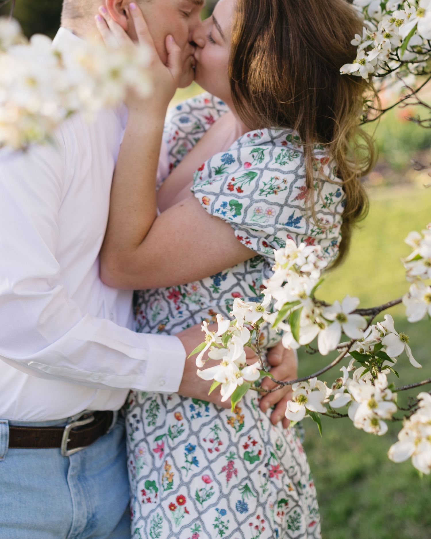 Sweet romantic poses in front of blooming white flowers during a spring photo session.