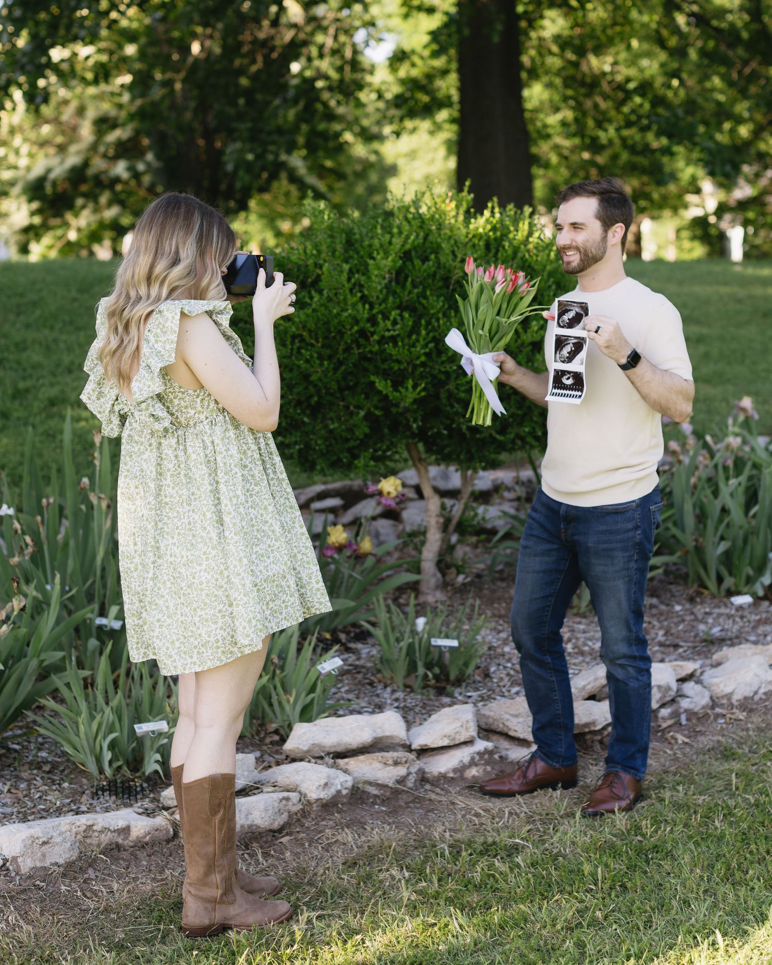 A couple sharing a special moment while holding ultrasound photos in a lush garden setting.