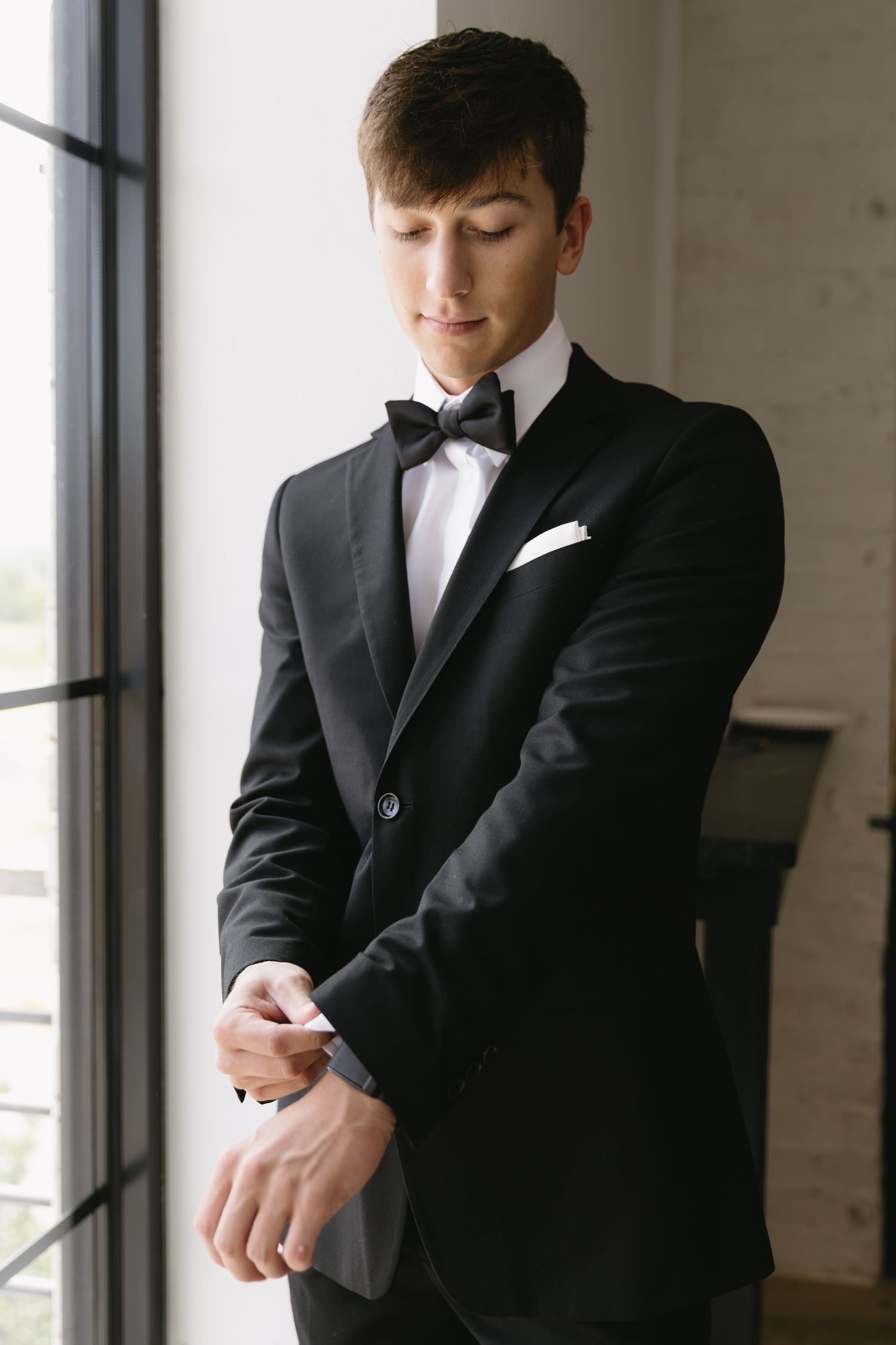 Wedding preparation scene showing formal black suit and tie adjustments.