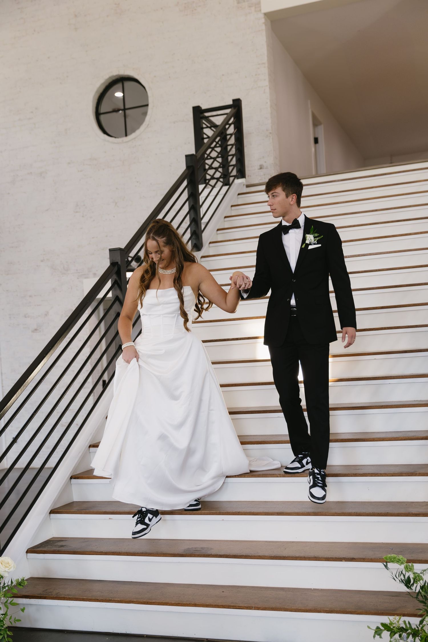 Couple in wedding attire posing playfully on white outdoor stairs.