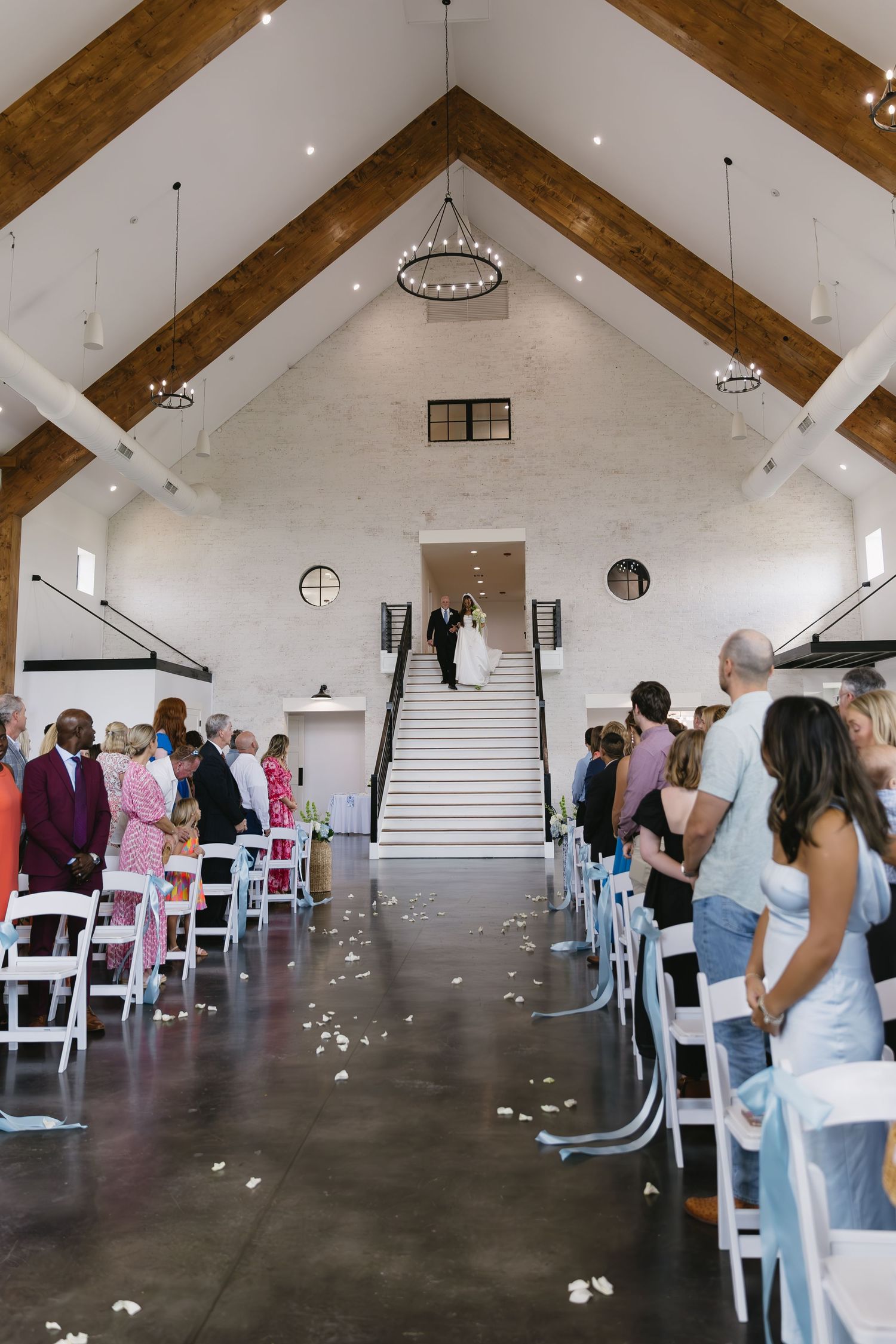 Modern wedding venue interior with white chairs and wooden beam ceiling details.