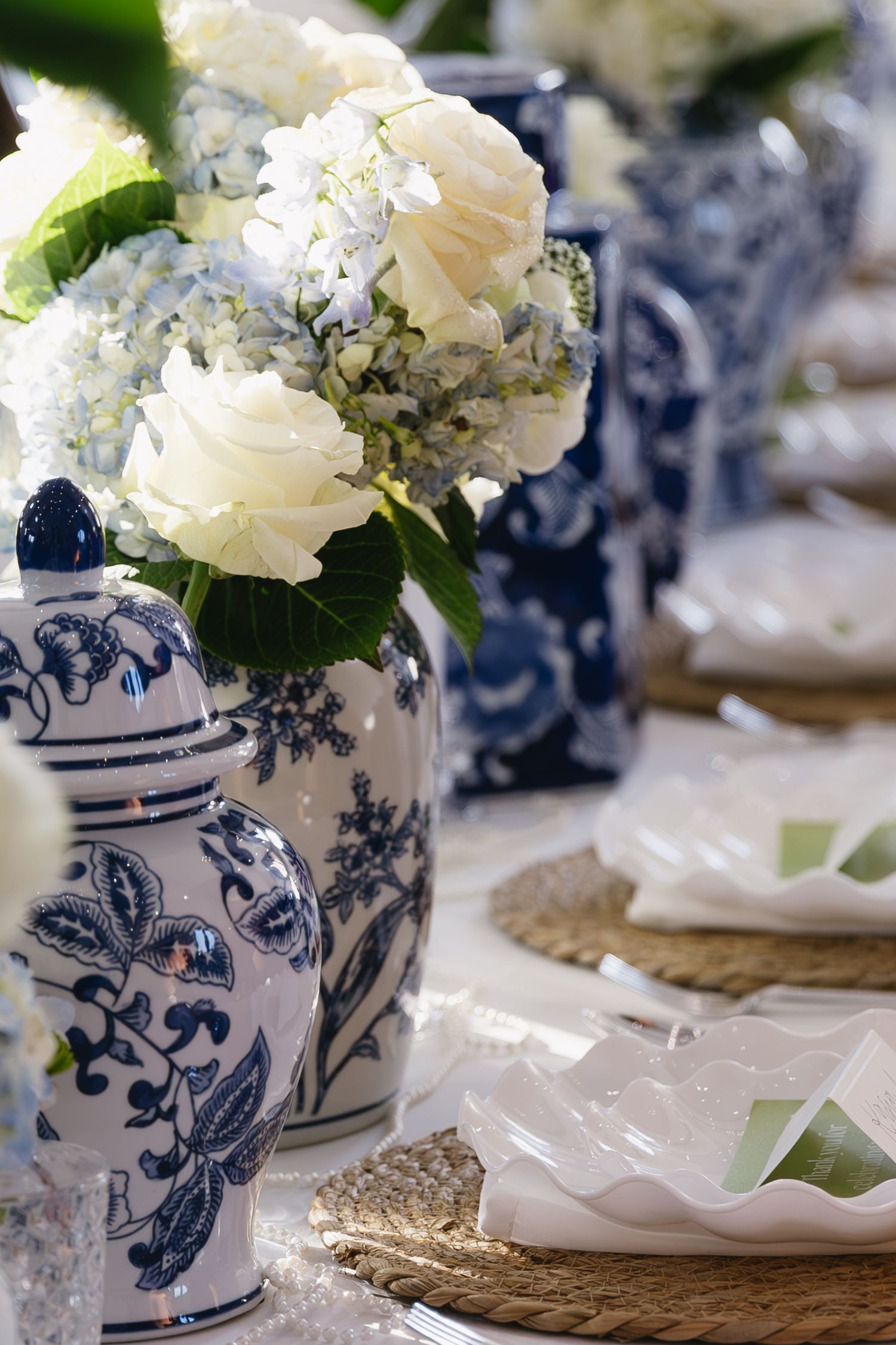 Blue and white ceramic vases filled with elegant white floral arrangements on a table setting.