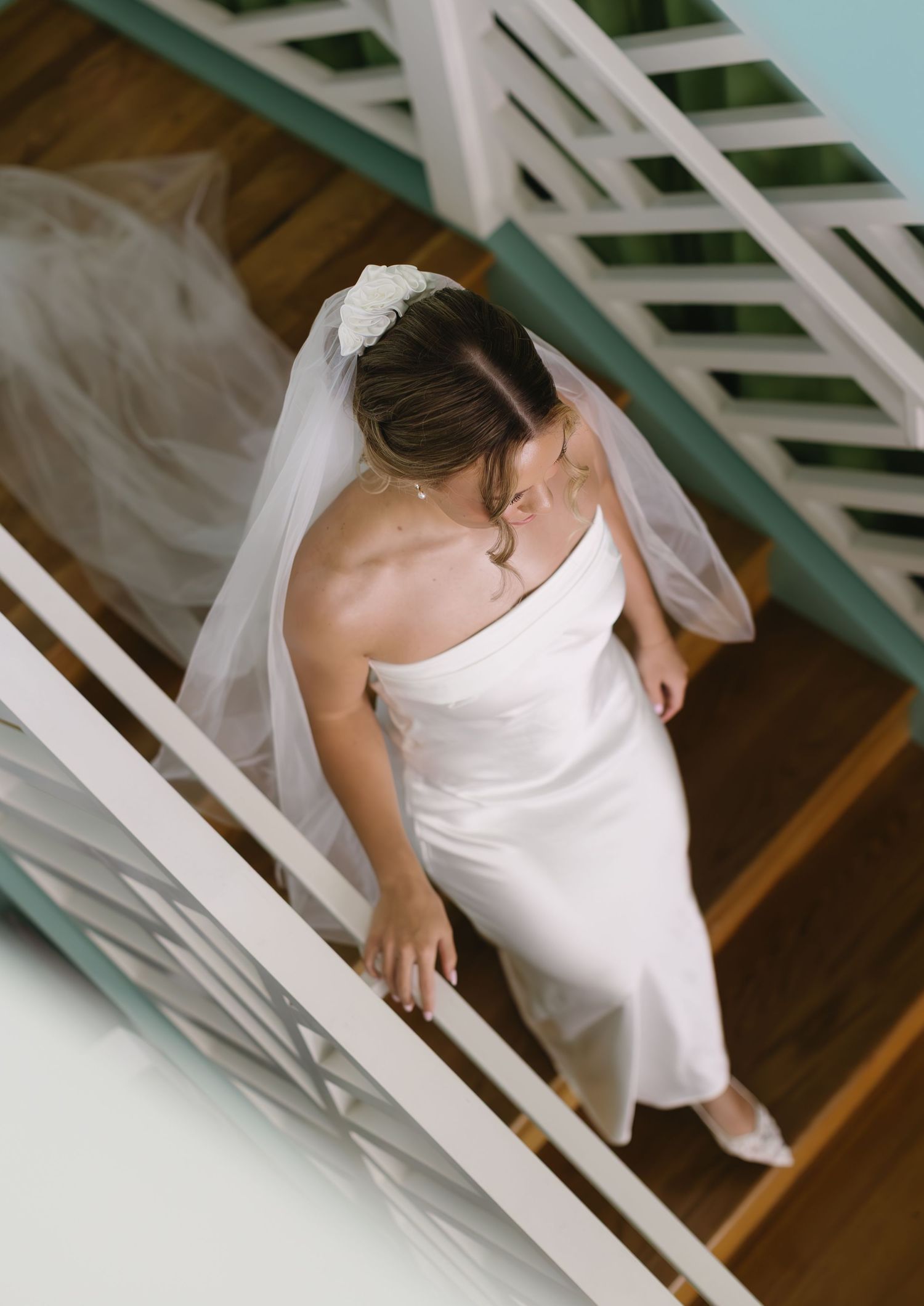 A close-up view of a white wedding dress descending down a wooden staircase.