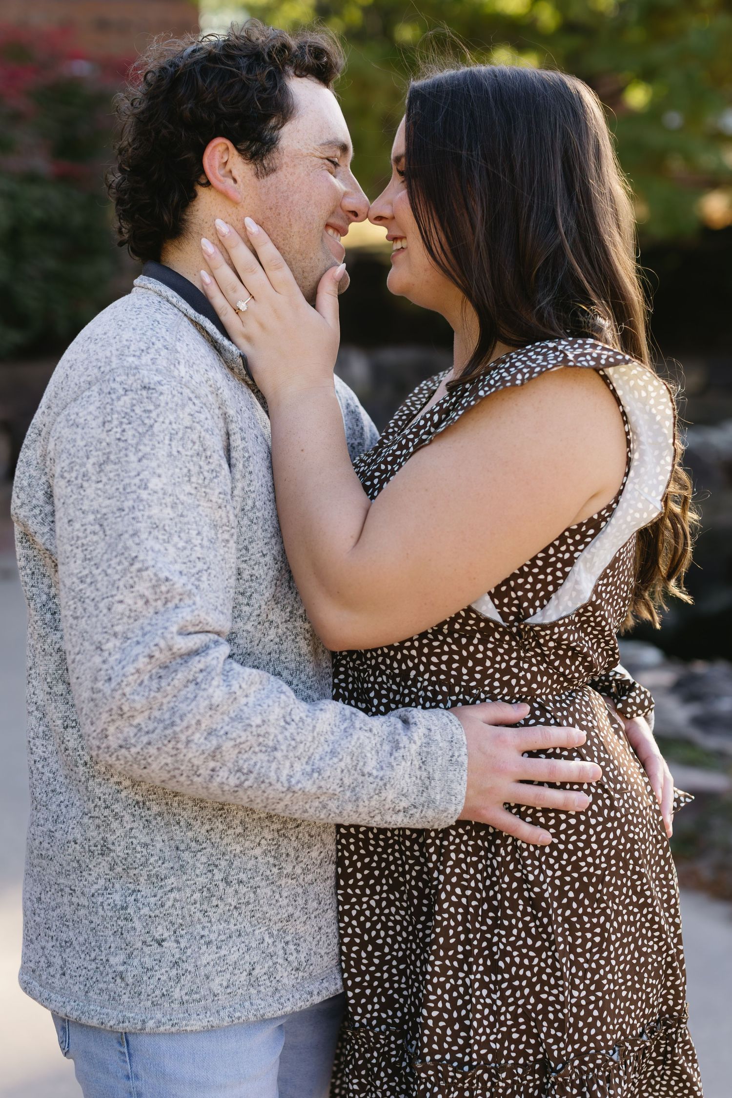 A couple embraces while wearing a gray sweater and polka dot dress during an outdoor photoshoot.