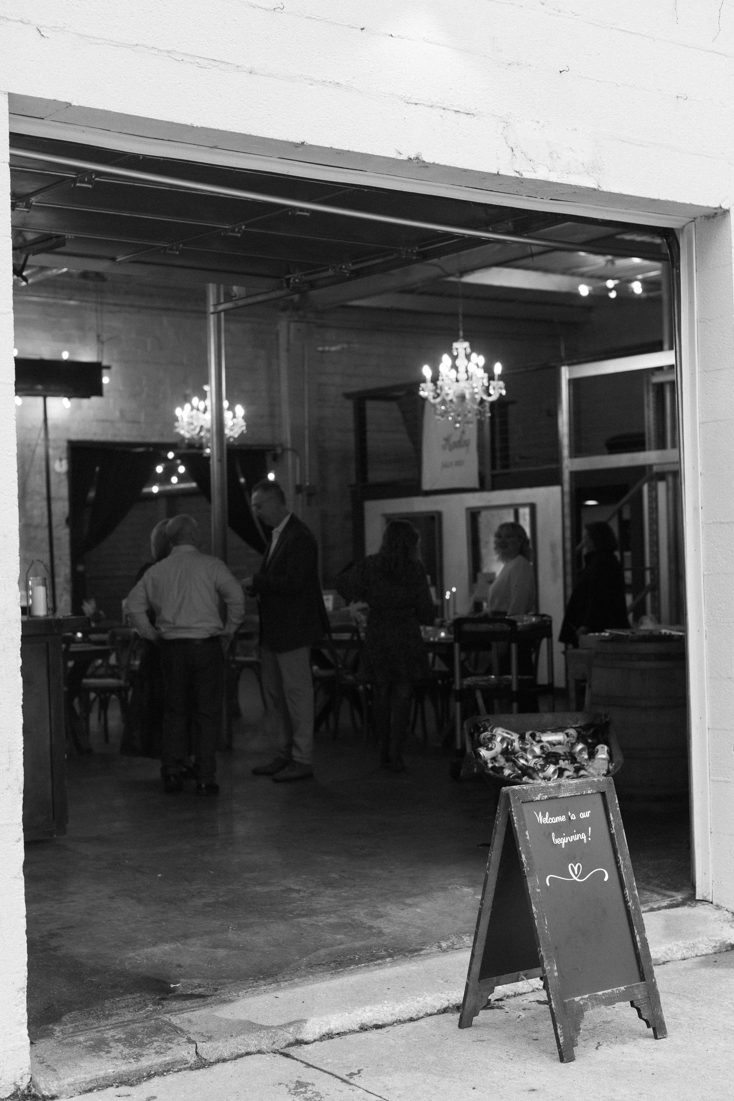Black and white interior view of an industrial space with chandeliers and signage.