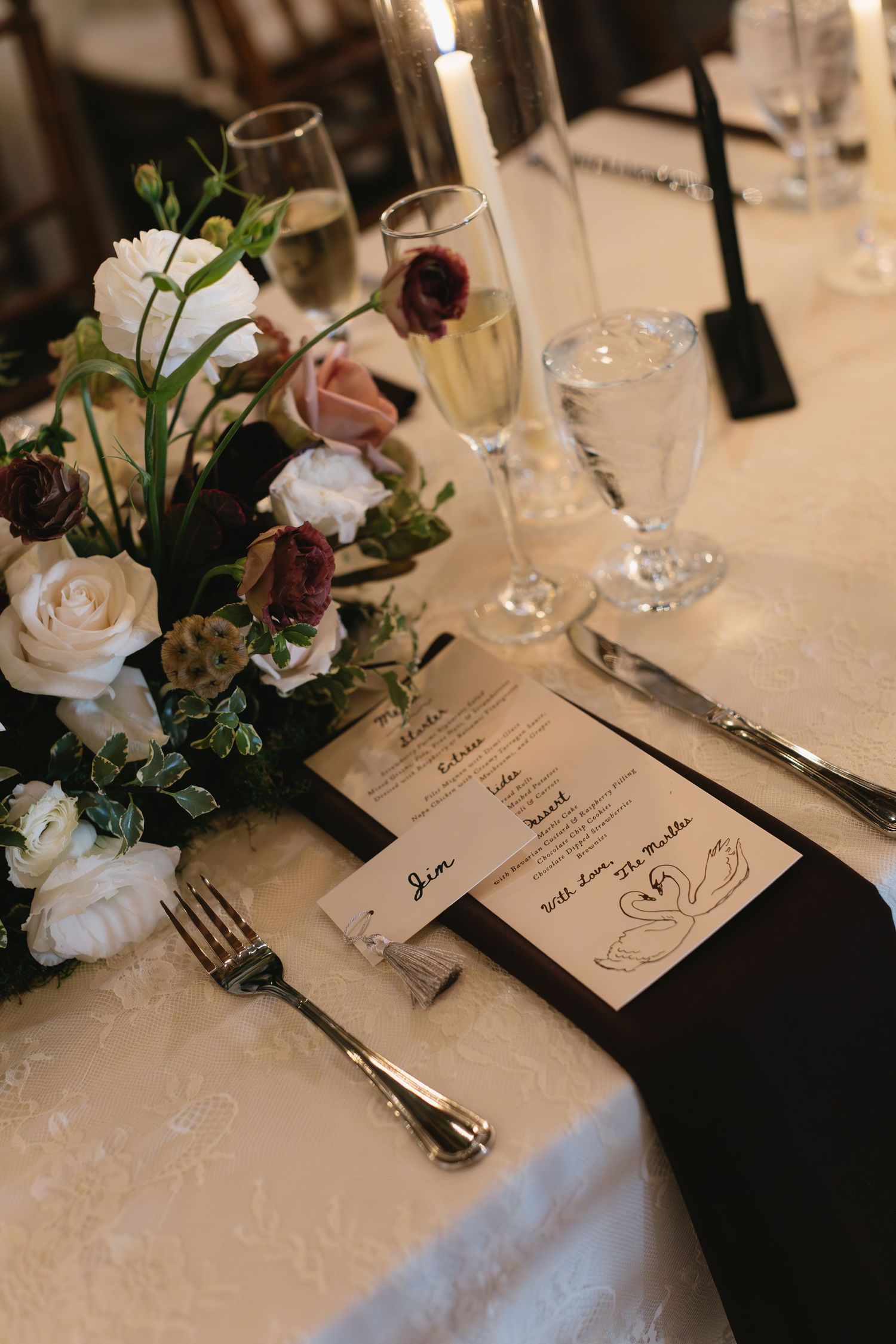Elegant wedding table setting with white roses, menu cards, and place settings on white linens.