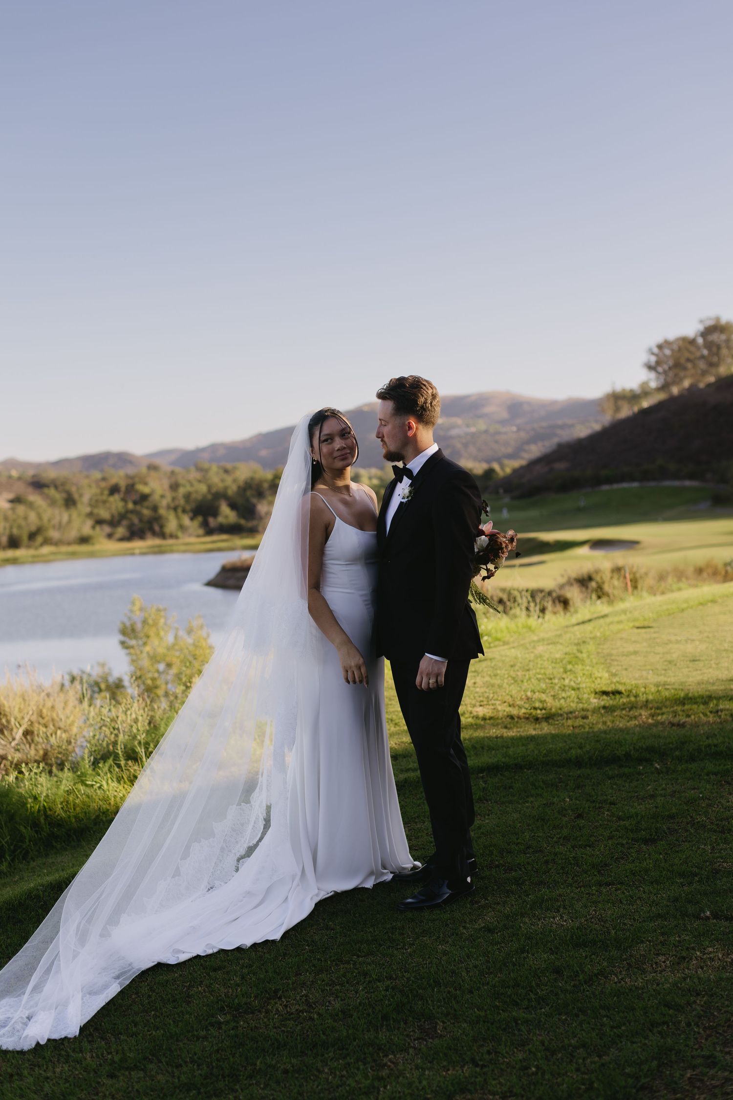 Scenic wedding photos of couple by lake with mountains and sunset in background.