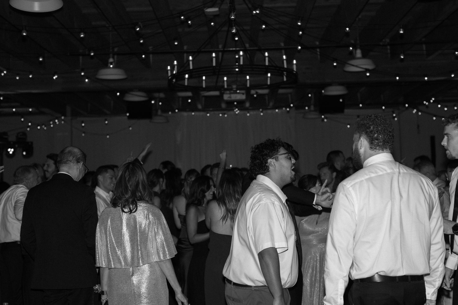 Dark reception hall with silhouettes of guests and string lights creating ambient atmosphere.