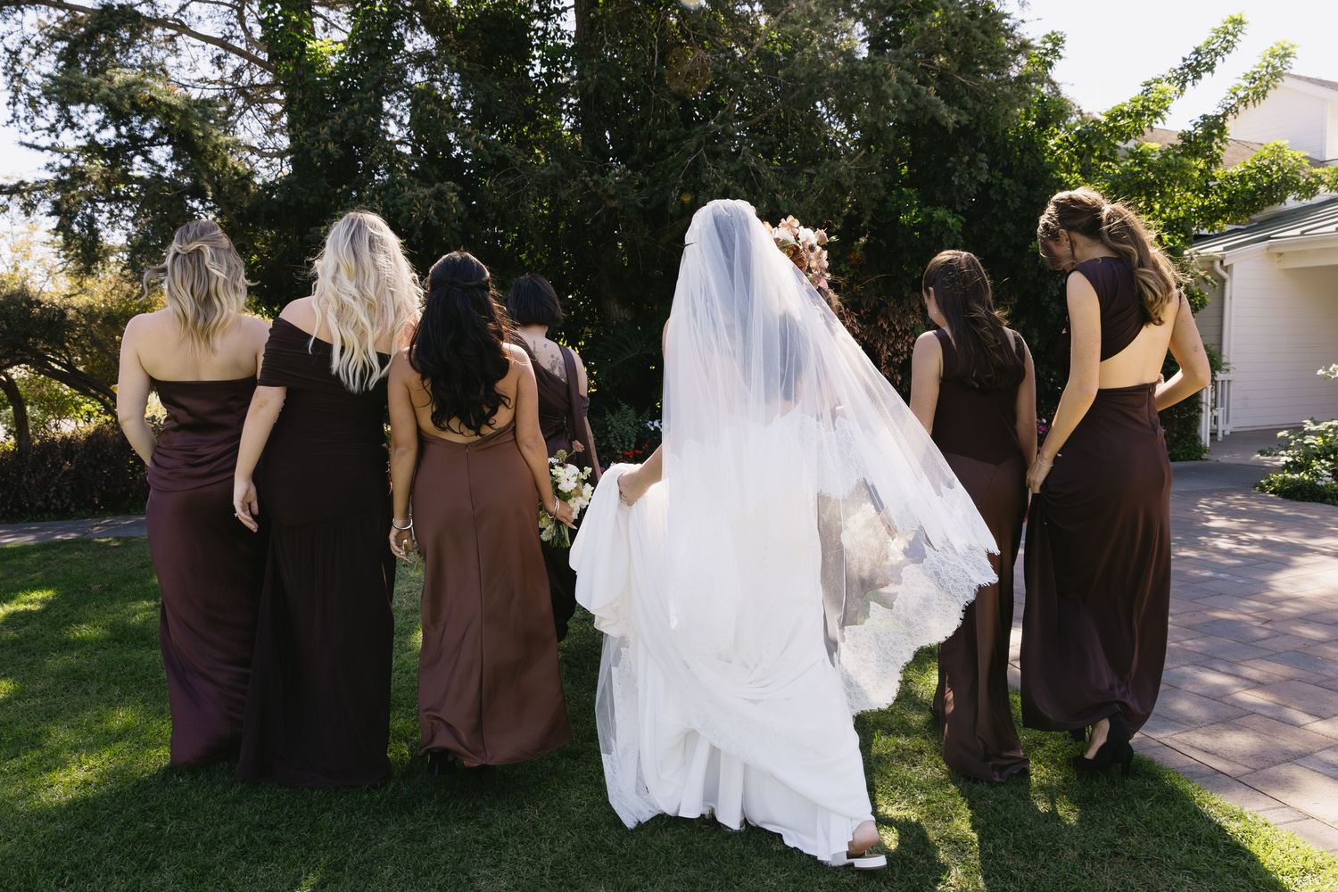 Wedding party in dark dresses walks together on garden path.