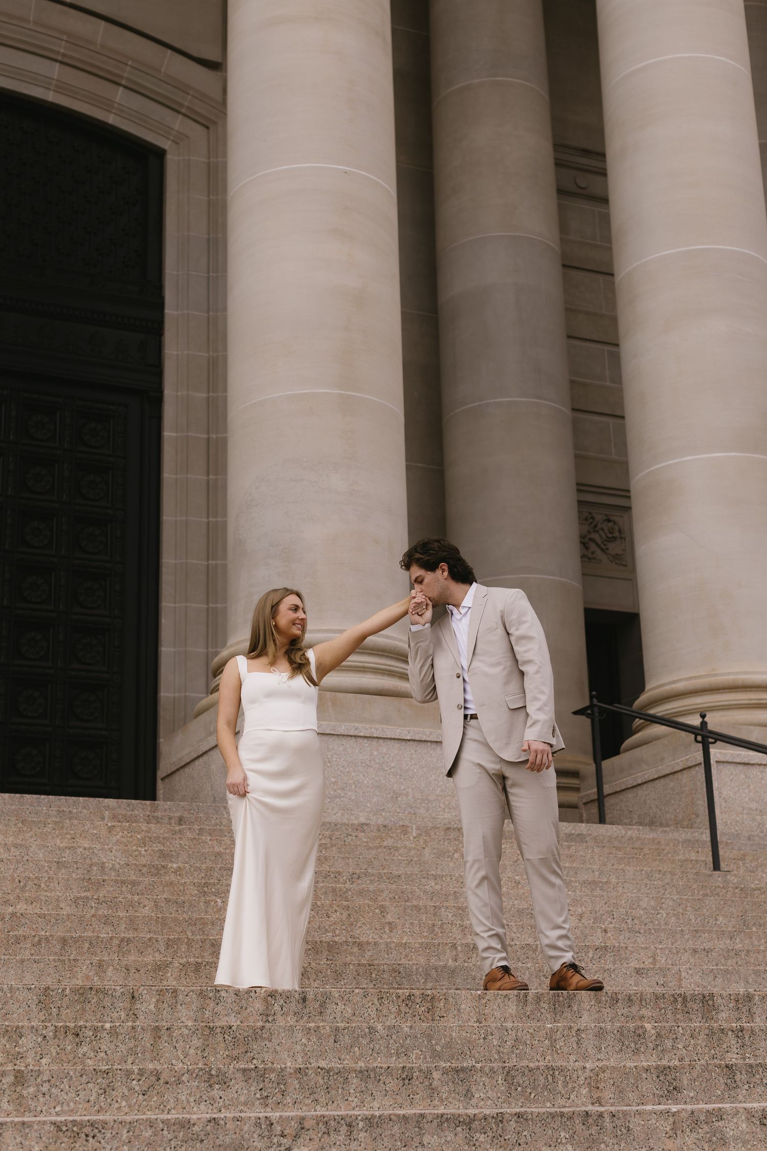 Romantic sequence of a couple in white attire interacting on elegant stone steps with columns.