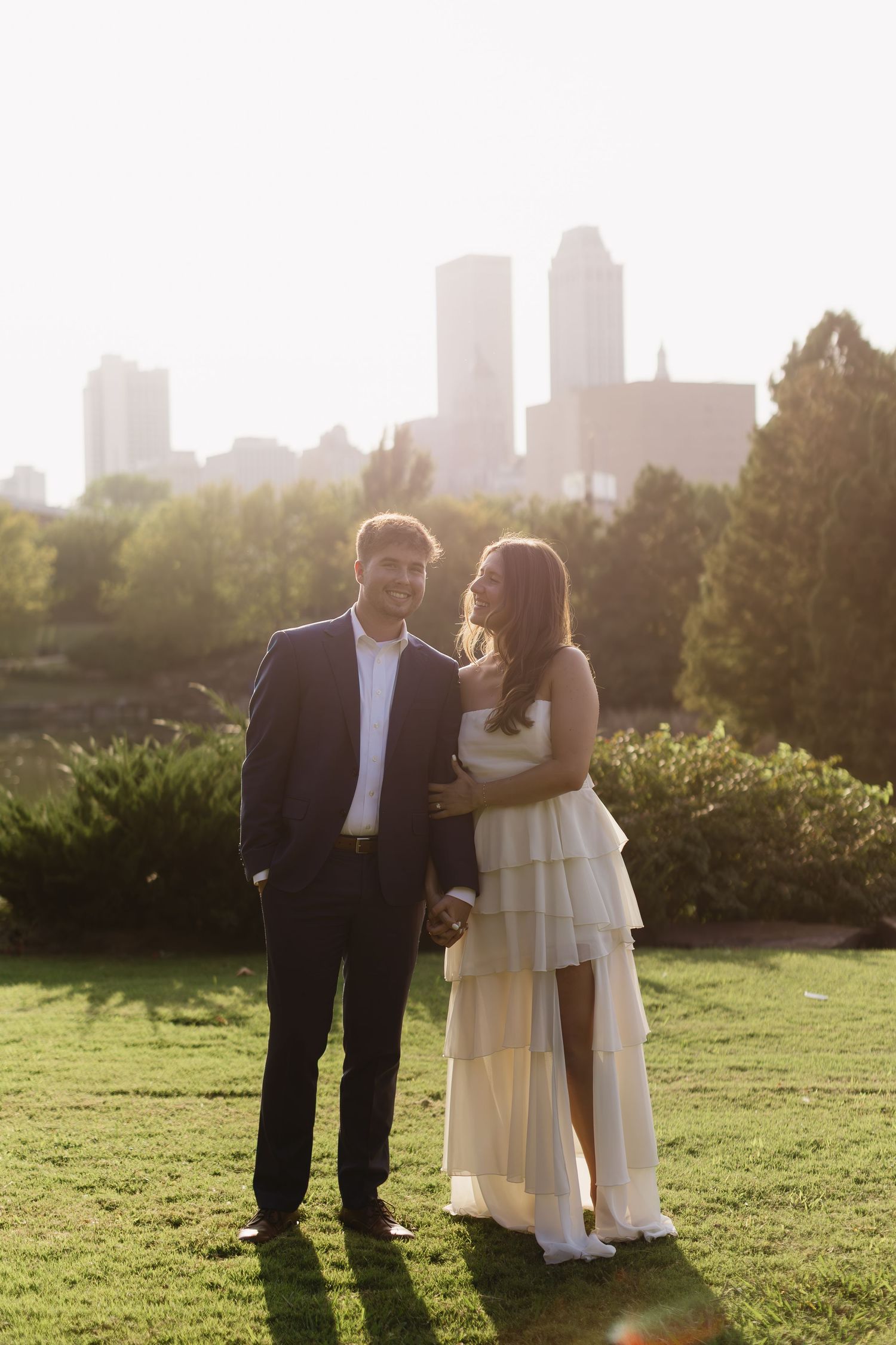 A sunset engagement photoshoot in a grassy park with city skyline in the background.