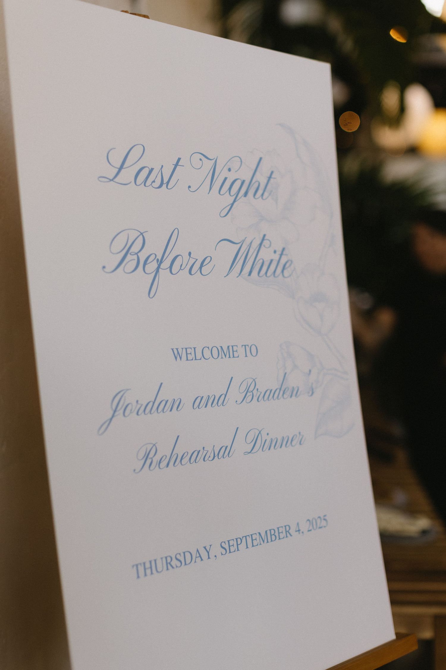 A wedding rehearsal dinner sign in blue calligraphy displays event details.