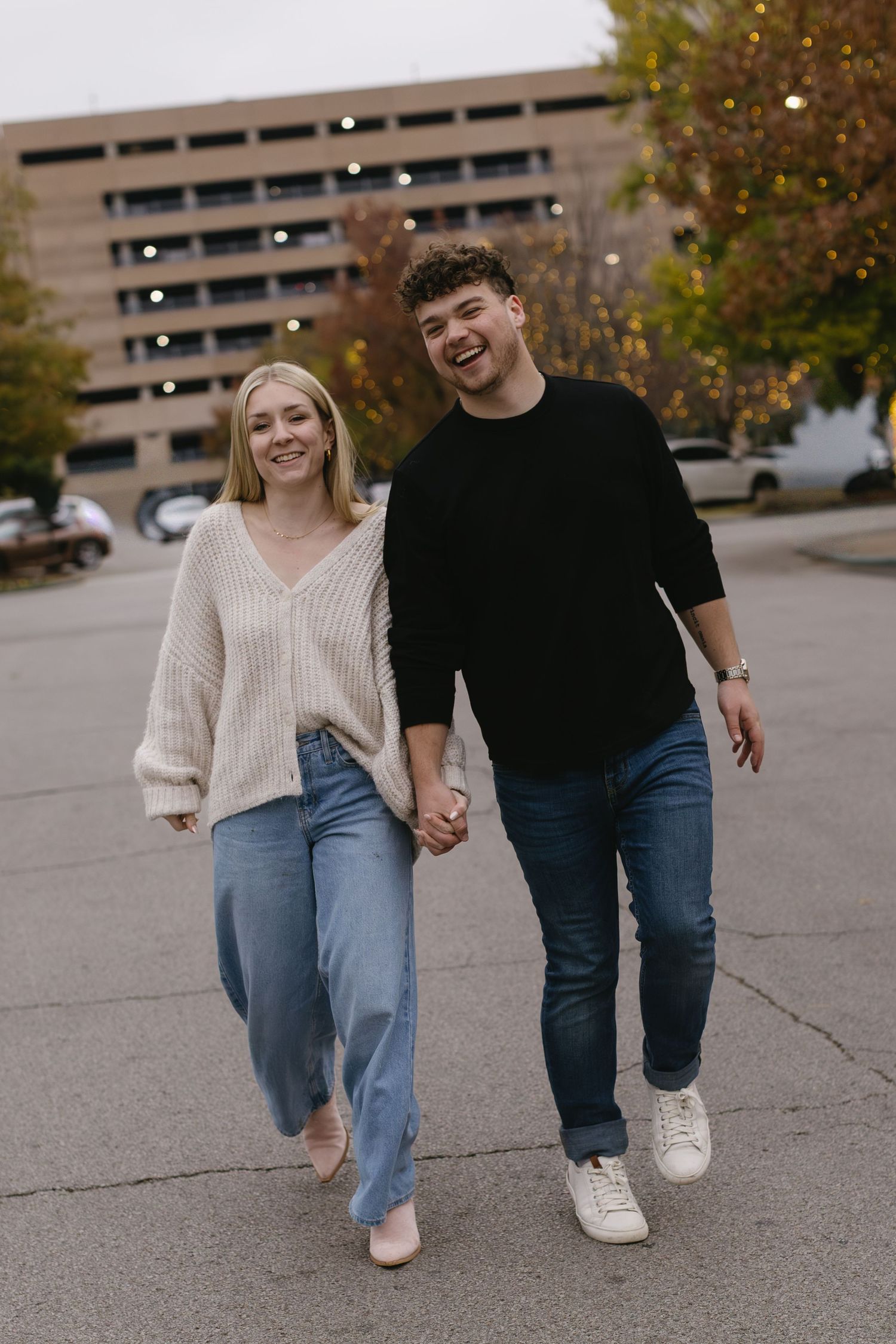 A couple in coordinating sweaters walking hand in hand through a parking lot in autumn.