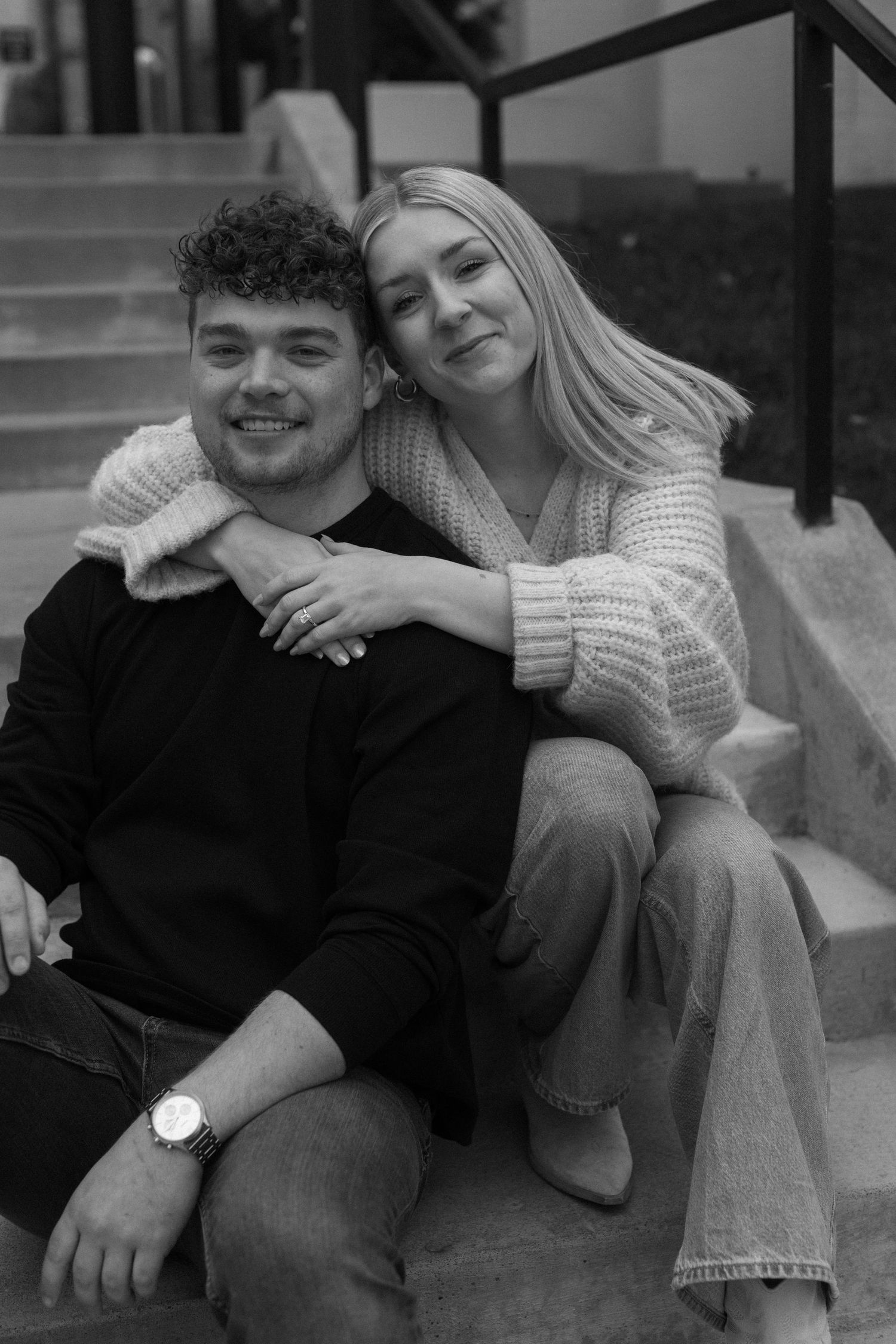 A couple in casual wear share intimate moments on outdoor steps in black and white photography.