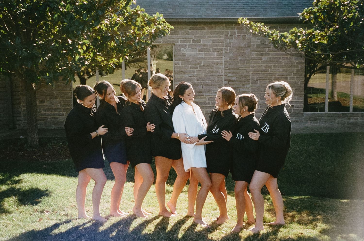 A line of bridesmaids in matching outfits posing together outdoors.