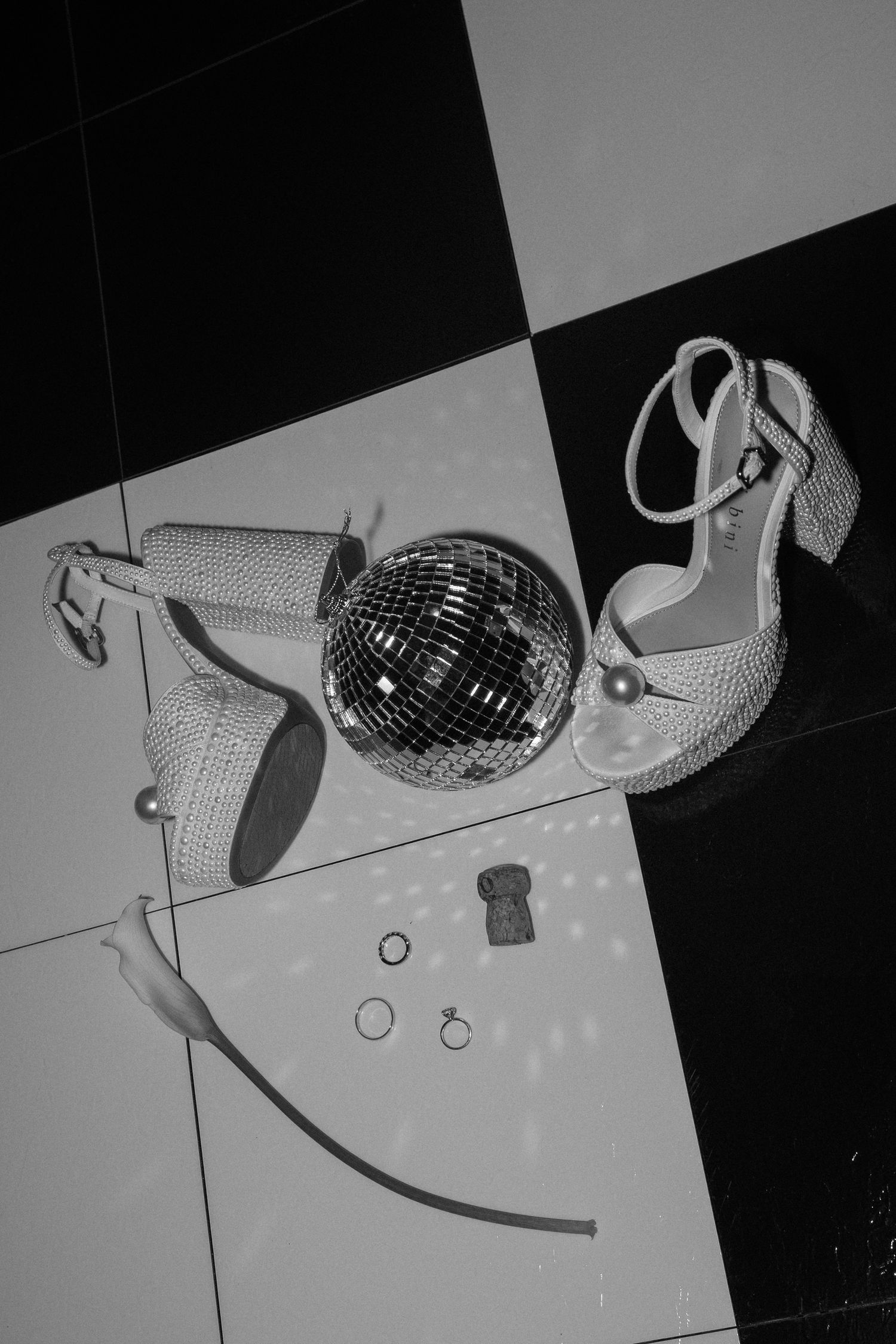 A disco ball and sparkly high heels arranged on a black and white checkered surface.