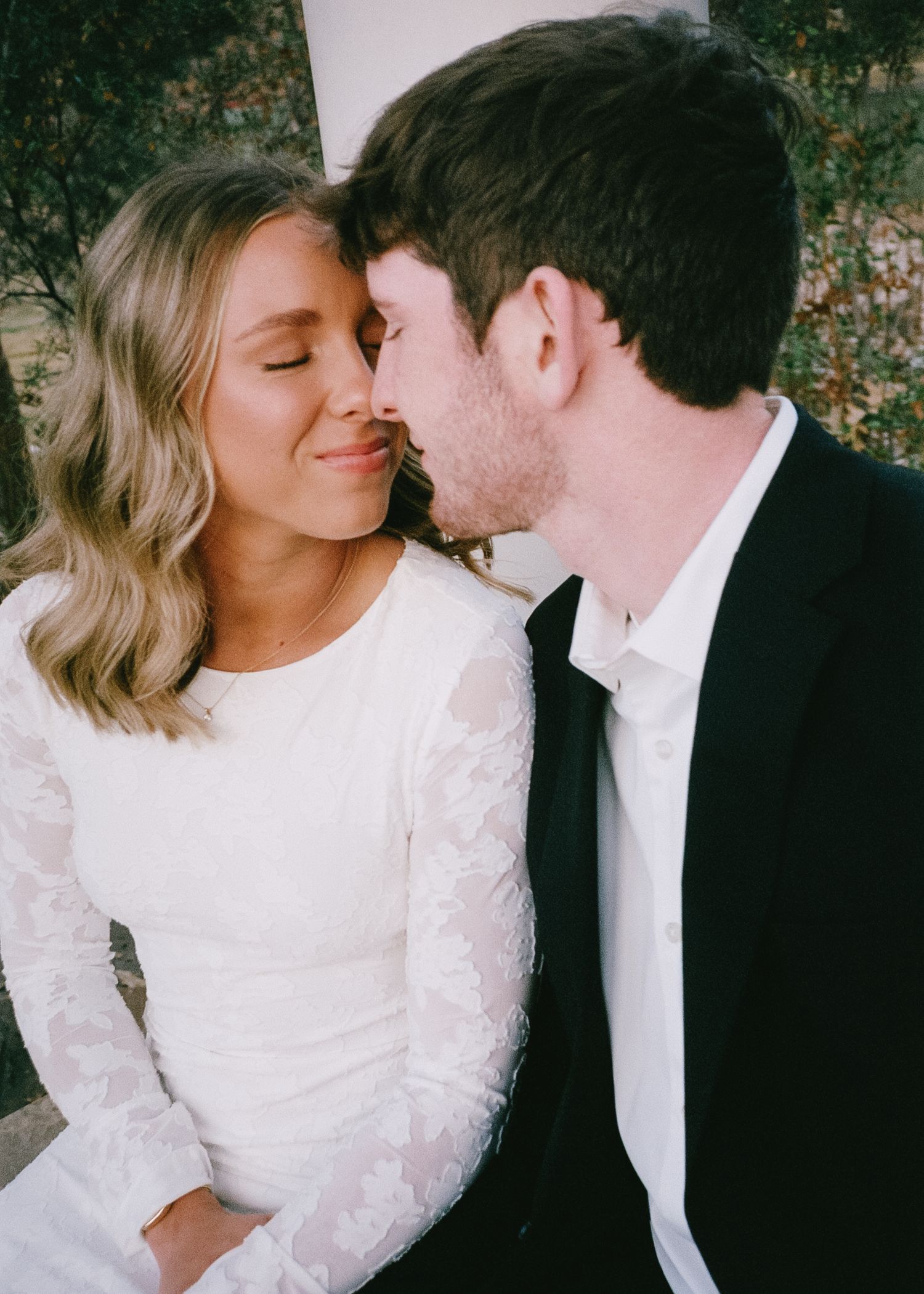 A romantic close-up moment between a couple in formal attire outdoors.