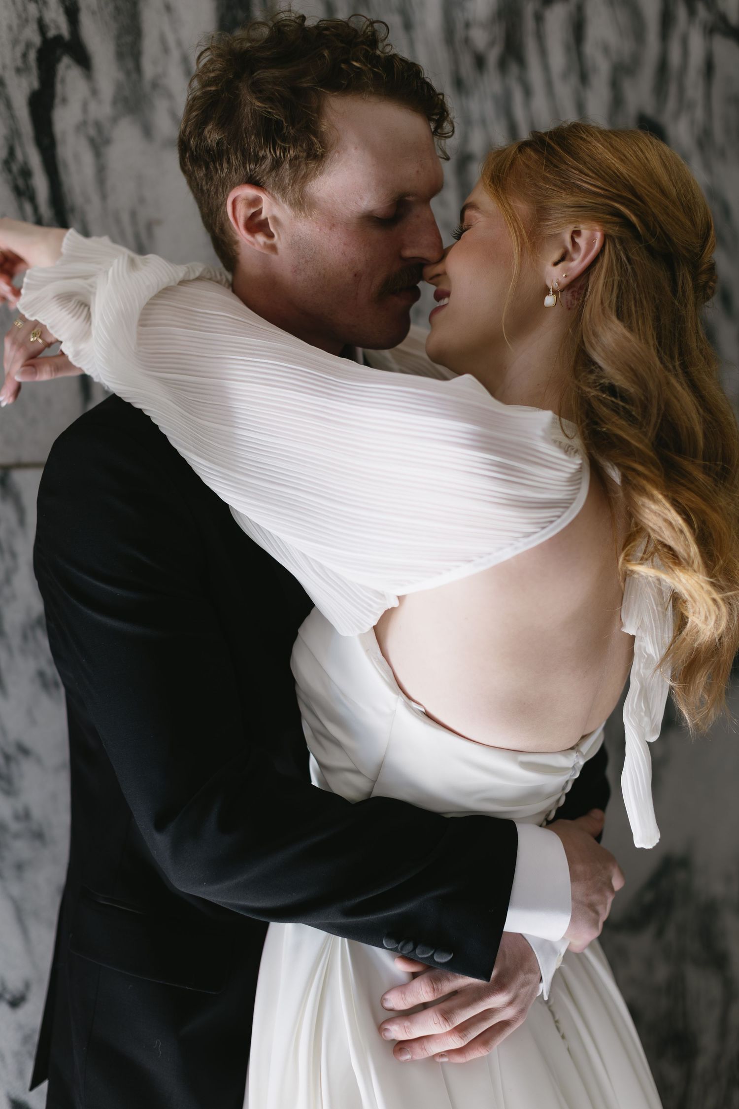 A tender moment between newlyweds as they dance together against a marble wall background.