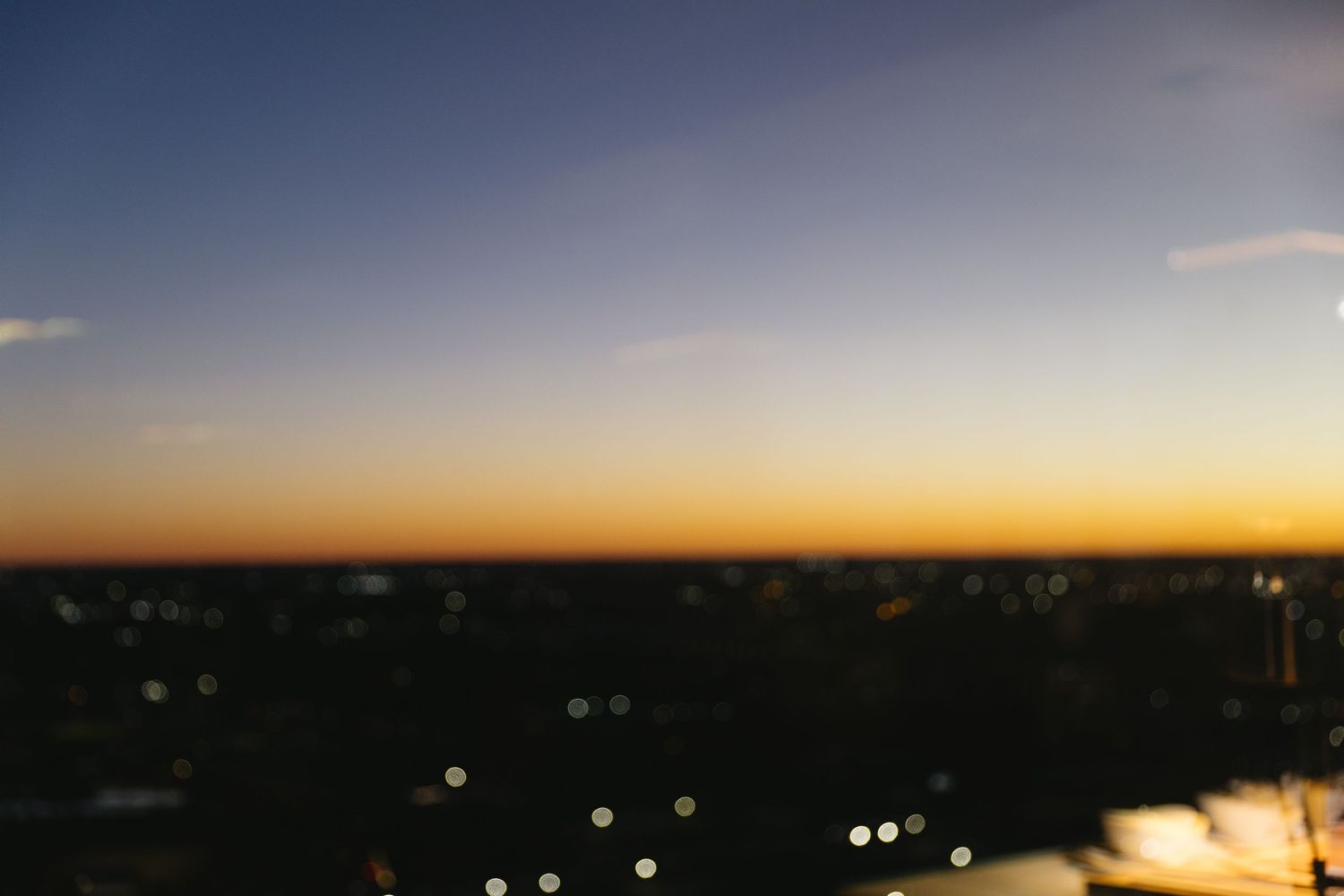 A scenic sunset skyline view with glowing orange horizon and twinkling city lights.