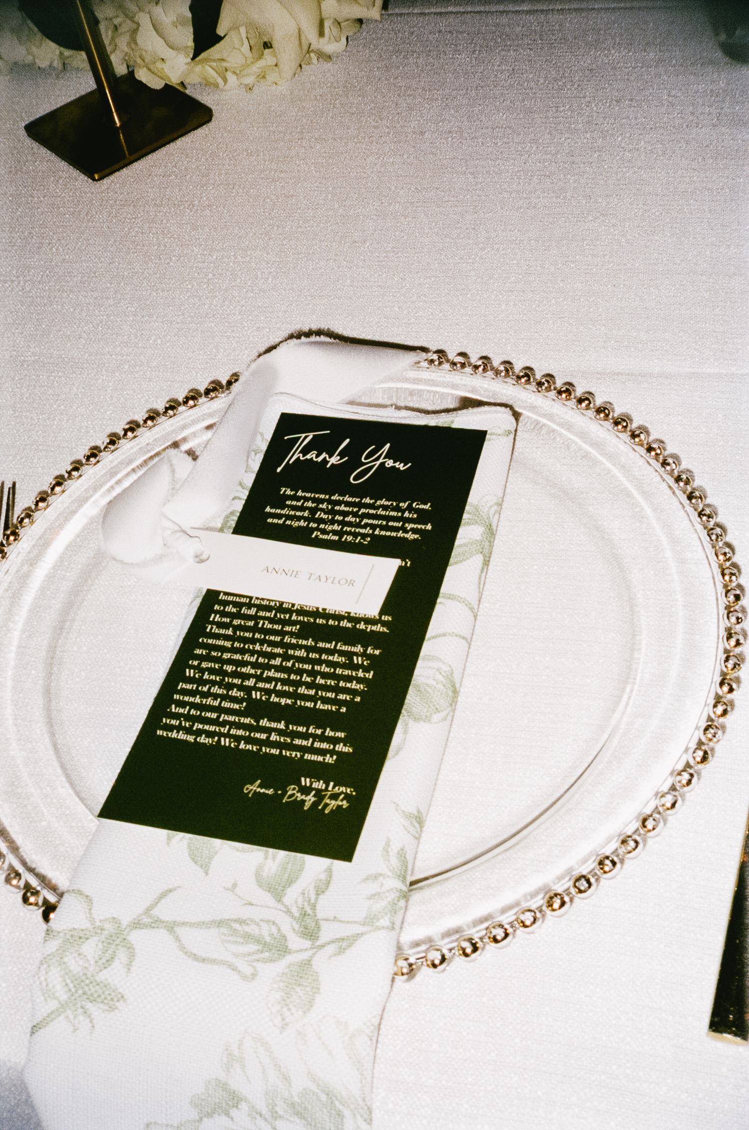 Black thank you note on marble plate with gold beaded charger and floral tablecloth.