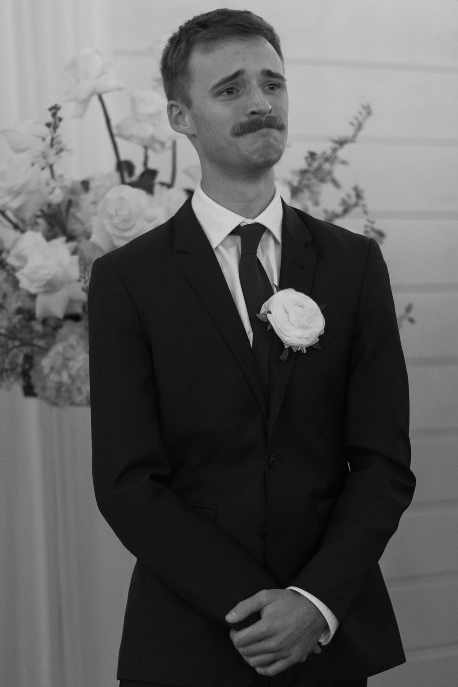 Black and white portrait of groom in formal suit with boutonniere showing emotional reaction.