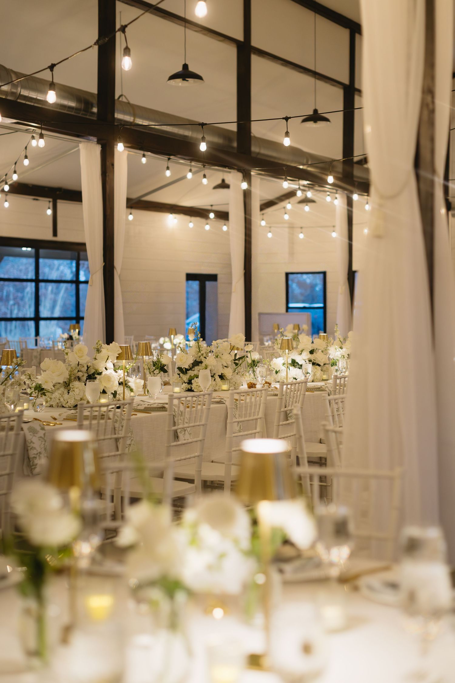 Elegant wedding reception venue with white table settings and hanging lights creating a romantic atmosphere.