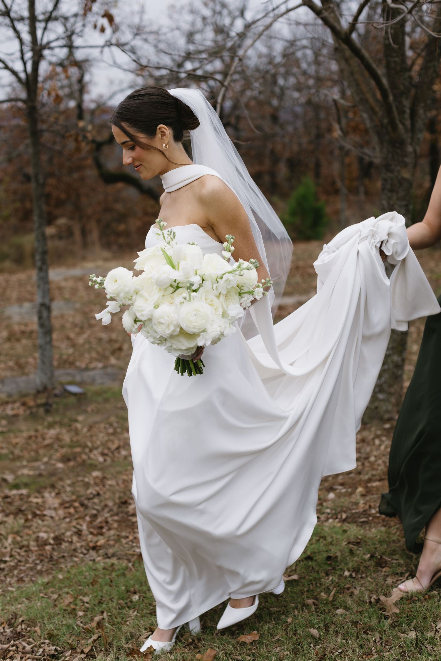 Bride in flowing white dress walks through fallen autumn leaves.