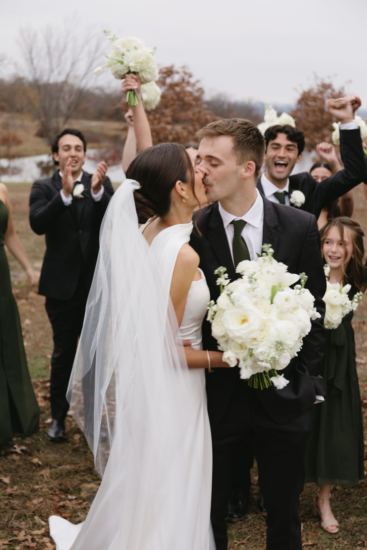 Wedding party celebrates outdoors with bride in white dress holding white bouquet.