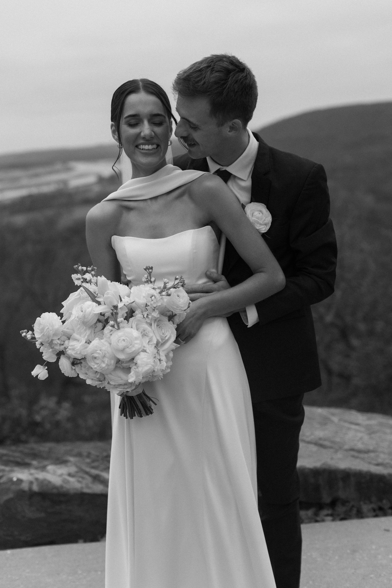 Black and white wedding portrait of couple embracing on a scenic overlook.