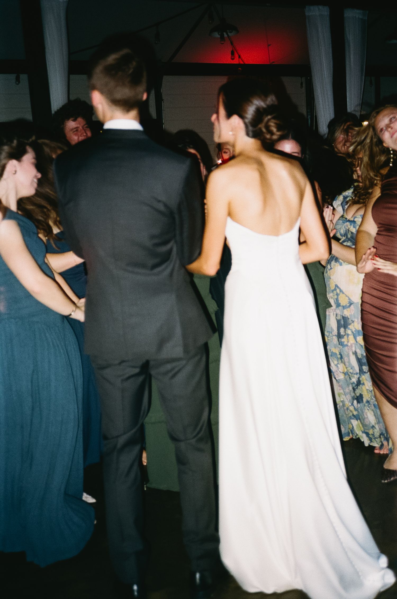 Candid reception photo showing wedding guests dancing in dim lighting.