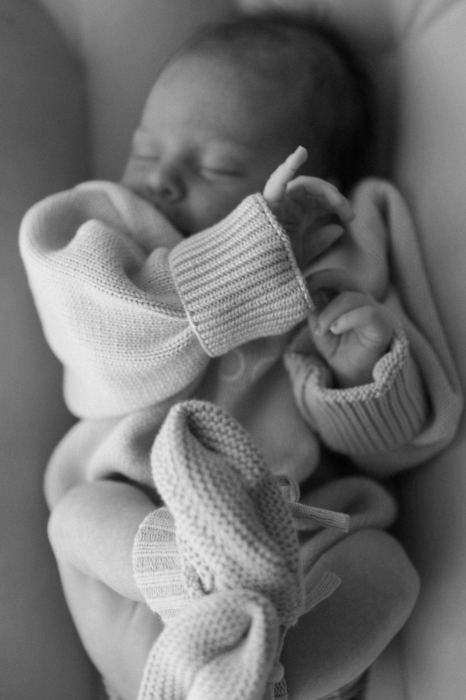 Black and white image of tiny knitted baby booties being held gently.