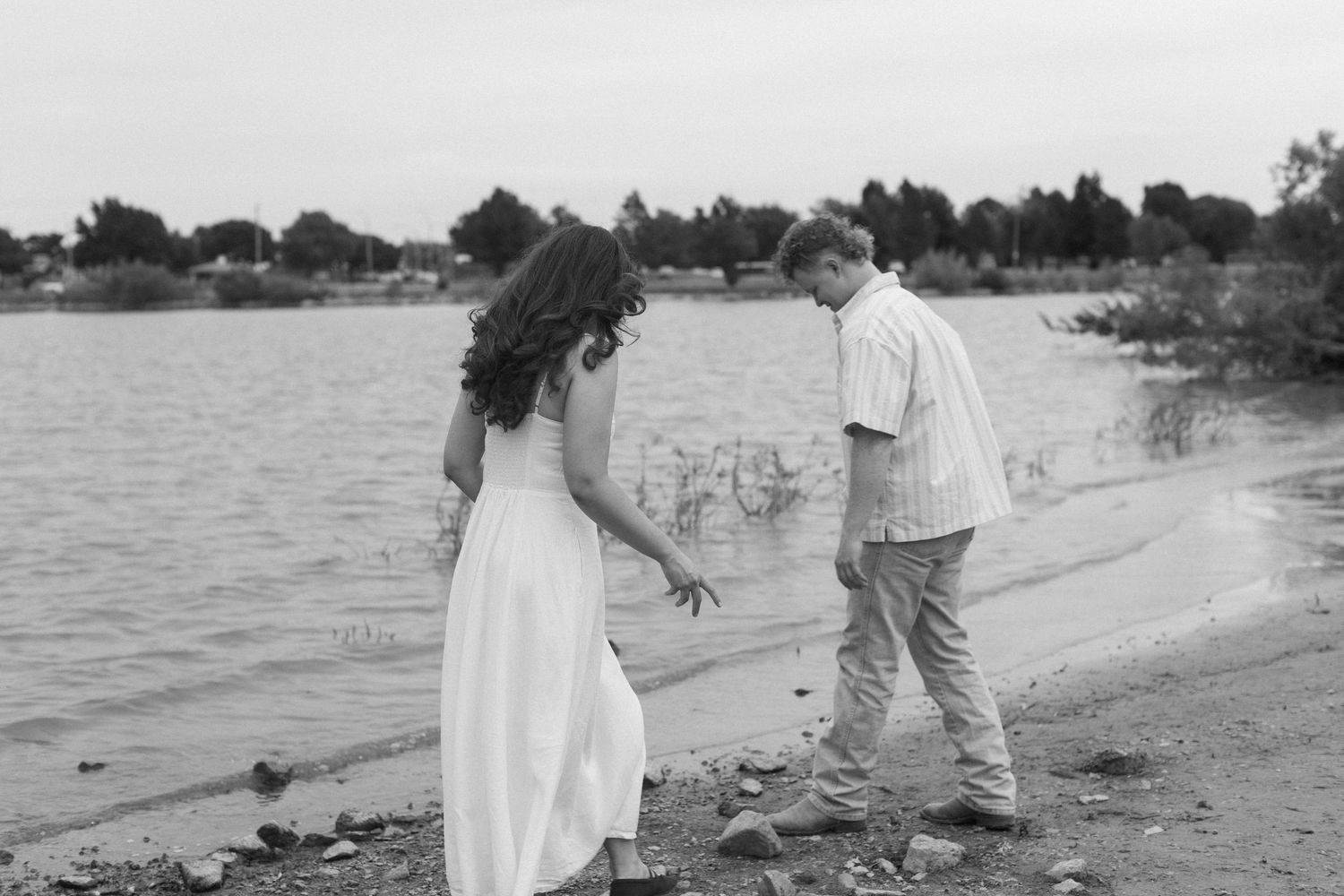 Couple taking a romantic stroll along a serene lakeside beach at sunset.