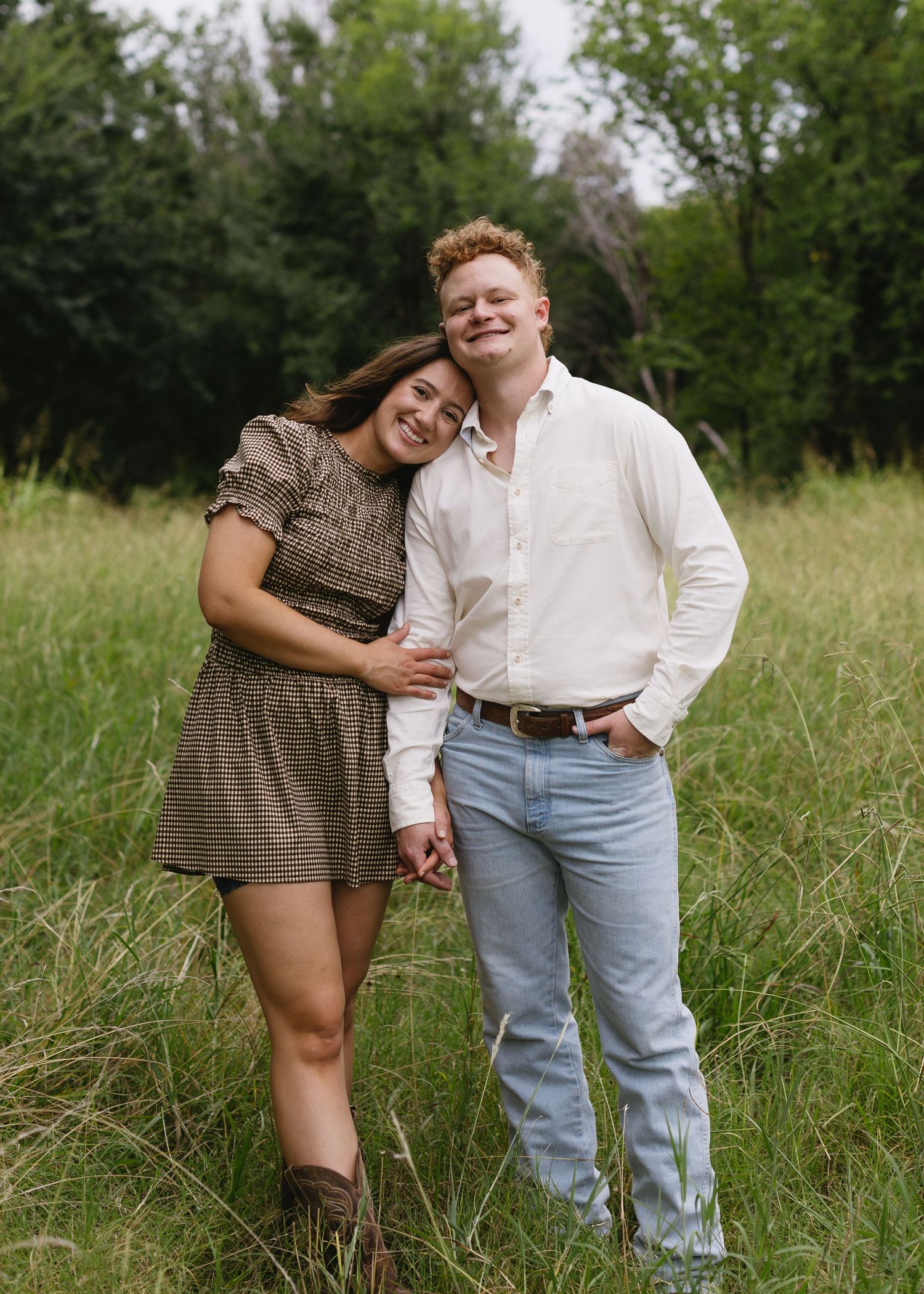 A romantic photoshoot in tall grass with two people in casual vintage-style clothing.