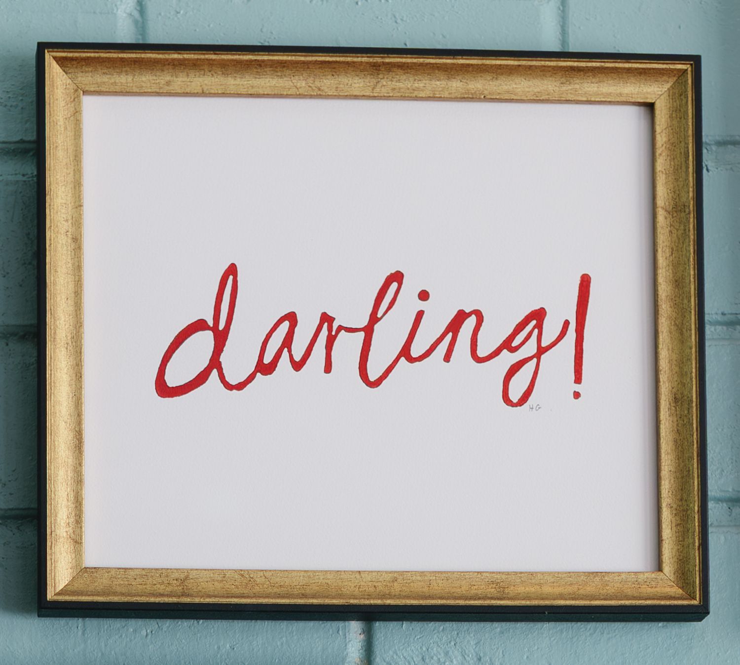 Three gold-framed artworks with red handwritten text mounted on a turquoise wall.