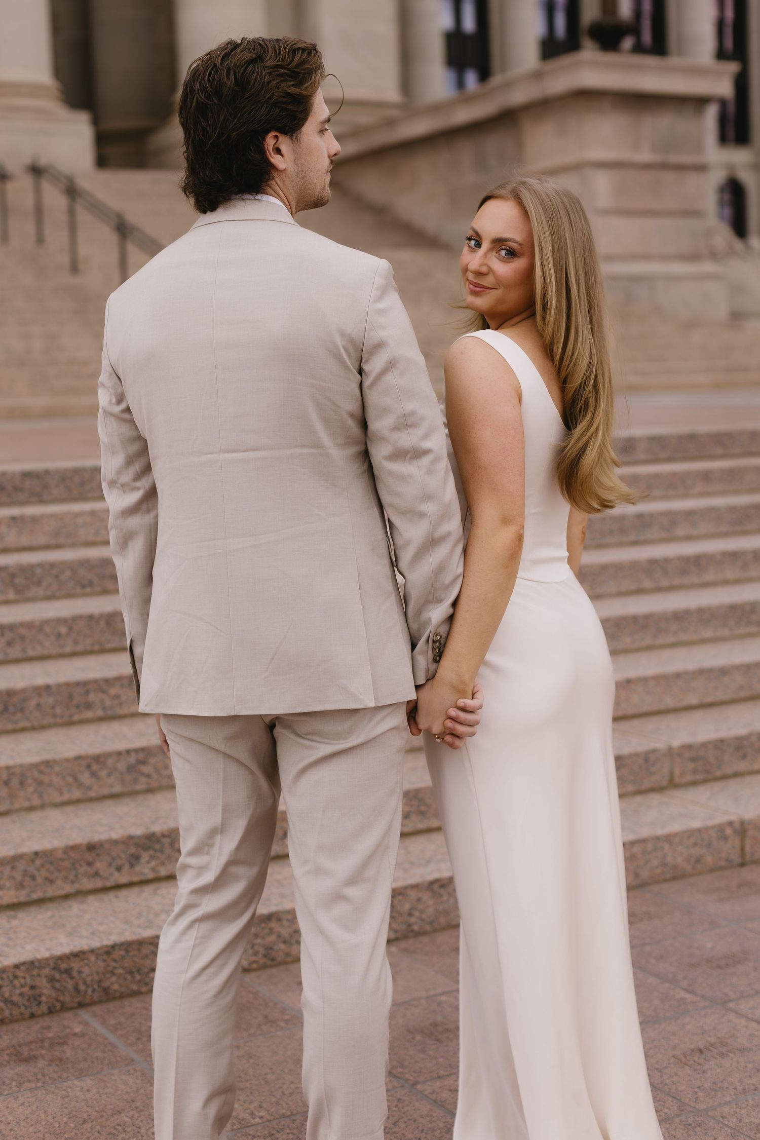 A couple stands together on stone steps outside a classical building.