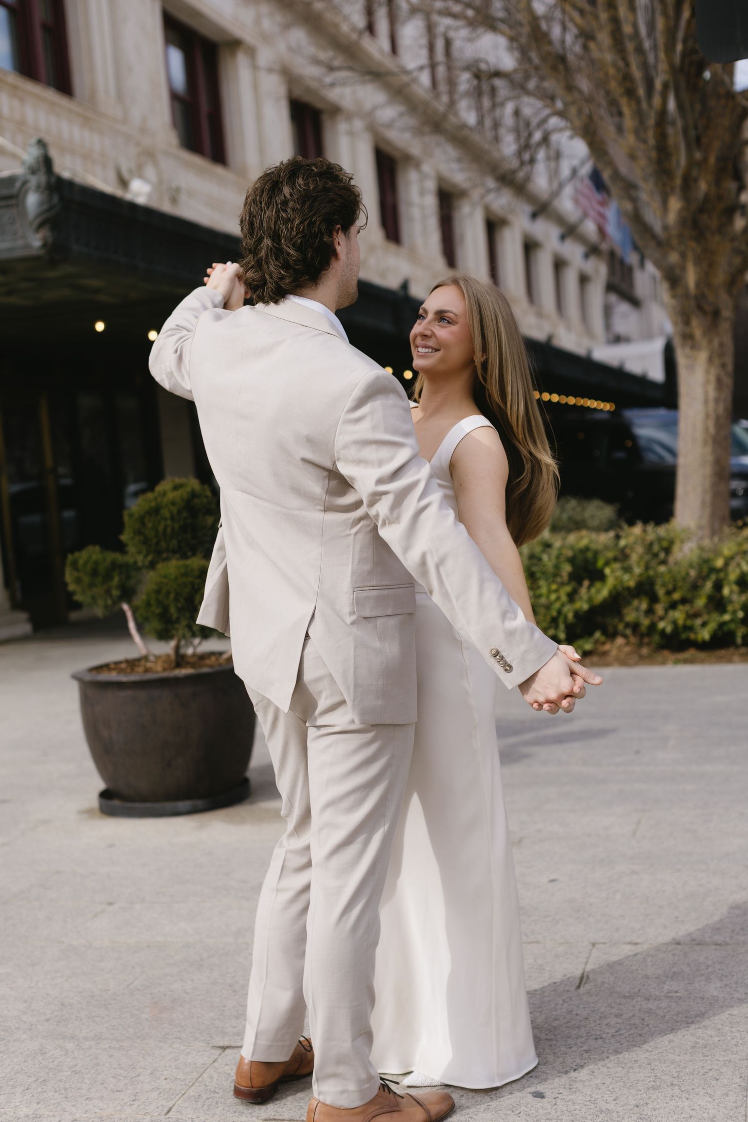Dancing couple in white and beige outfits share playful moments on an urban sidewalk.