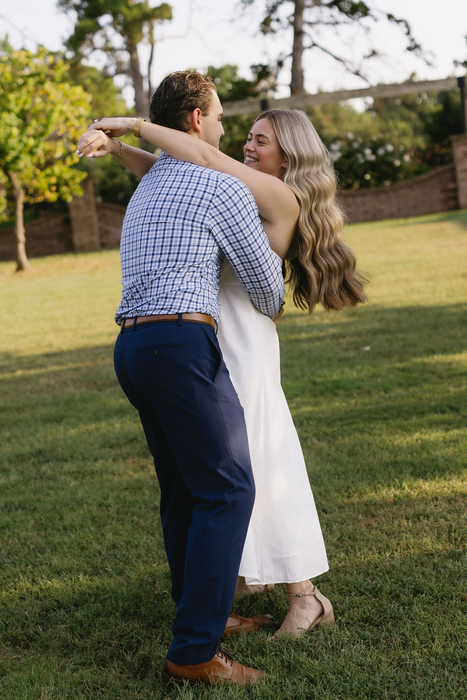 Playful couple dances on grassy lawn during golden hour photoshoot.