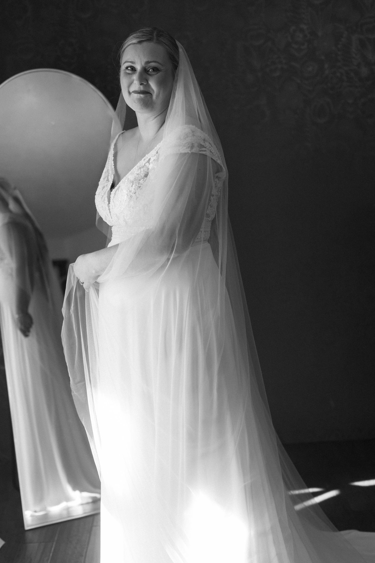 Elegant white wedding dress with flowing veil captured in dramatic black and white photography.