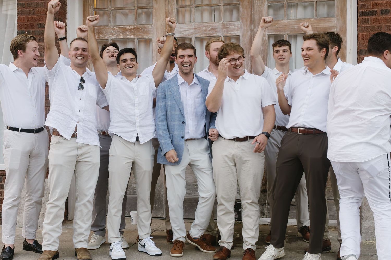 A group of men in white and light colored outfits laughing and posing together at a formal event.