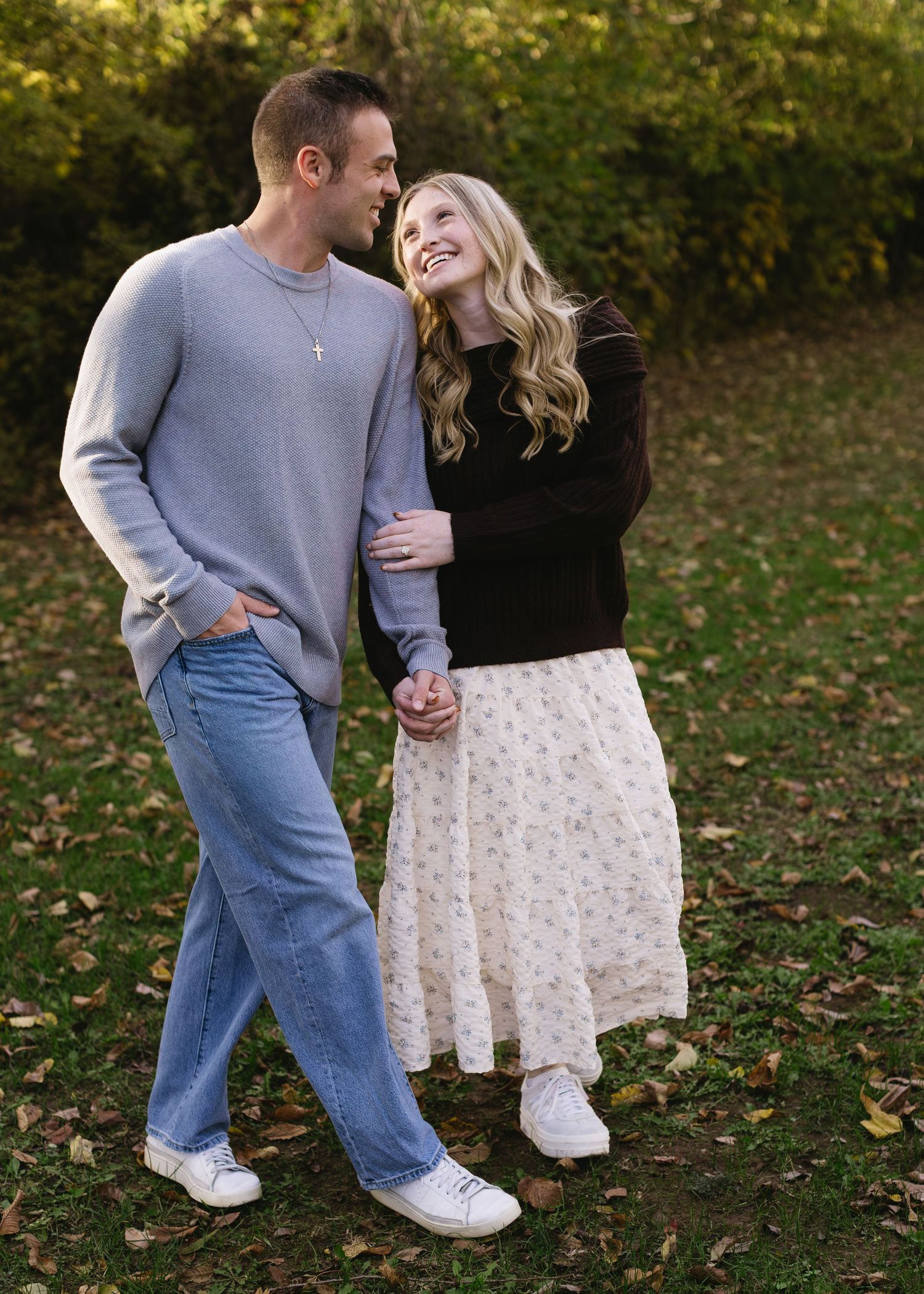 A couple shares an intimate moment while walking through fallen autumn leaves in a park.