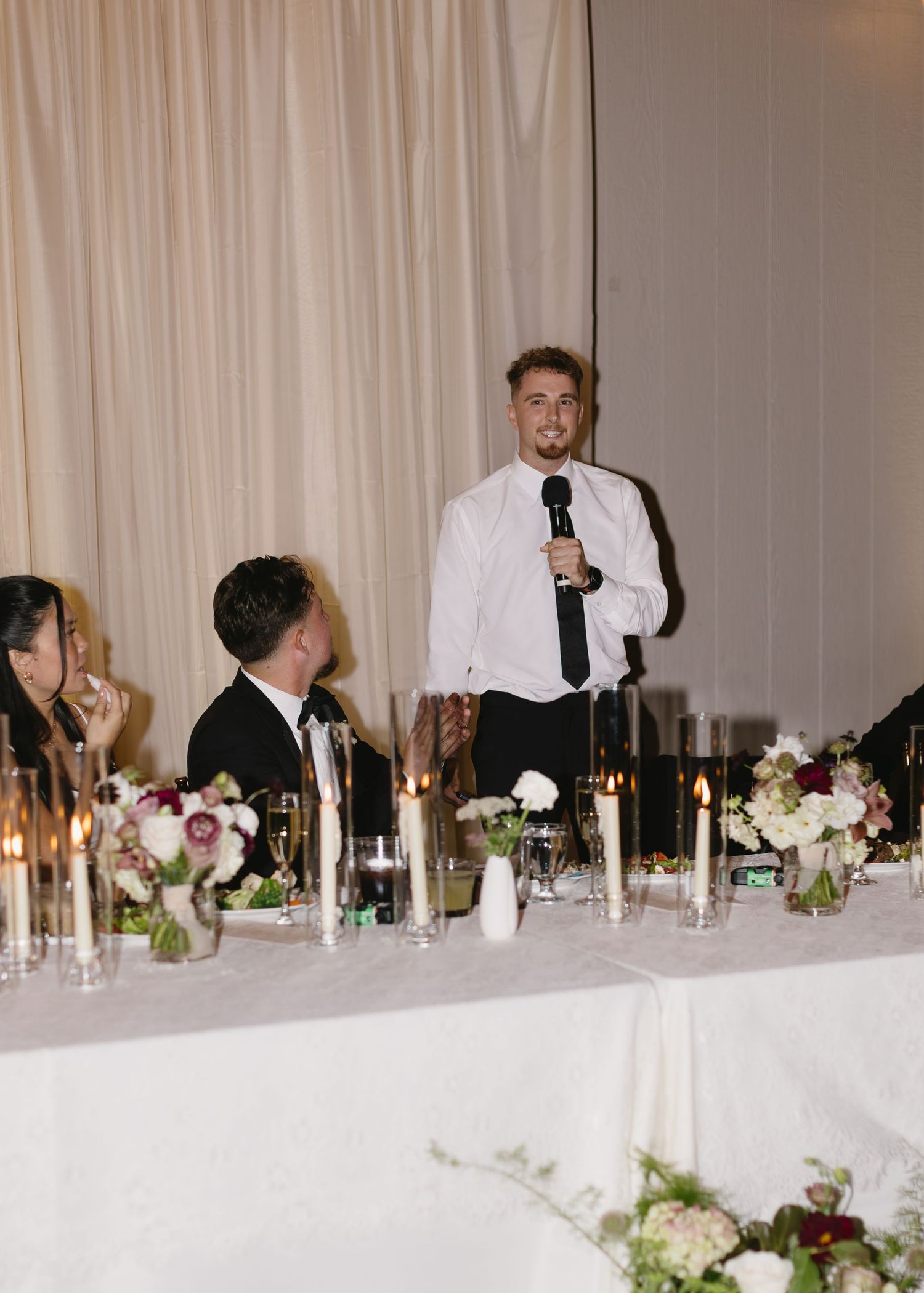 Reception guests mingling at decorated head table with floral centerpieces.