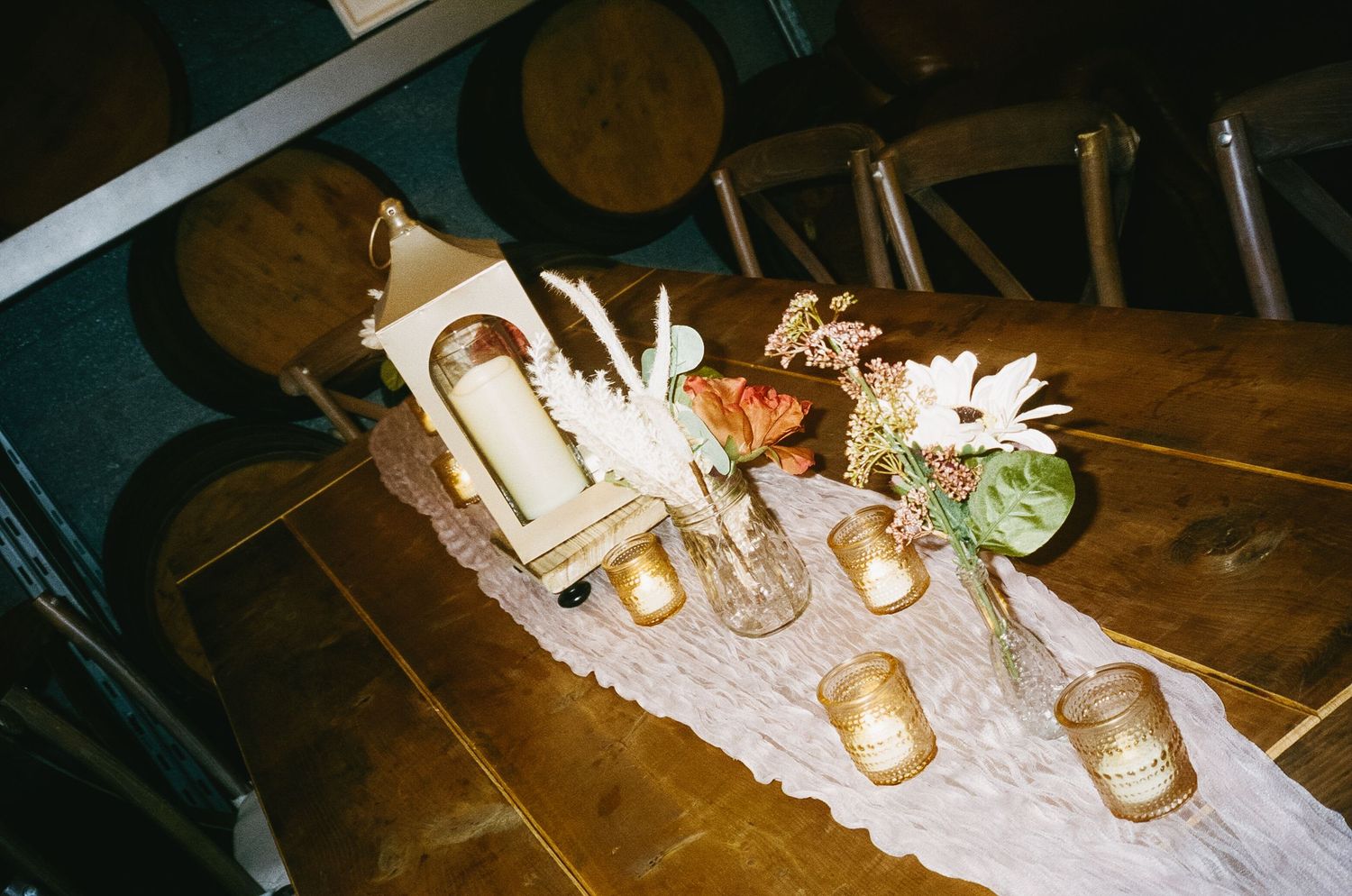 Wedding reception table decorated with candles and flowers against rustic barrel backdrop.