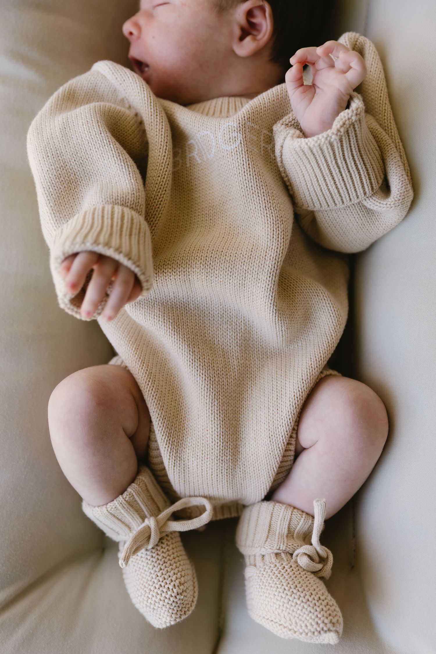 Infant wearing cozy cream-colored knit sweater and booties on white background.