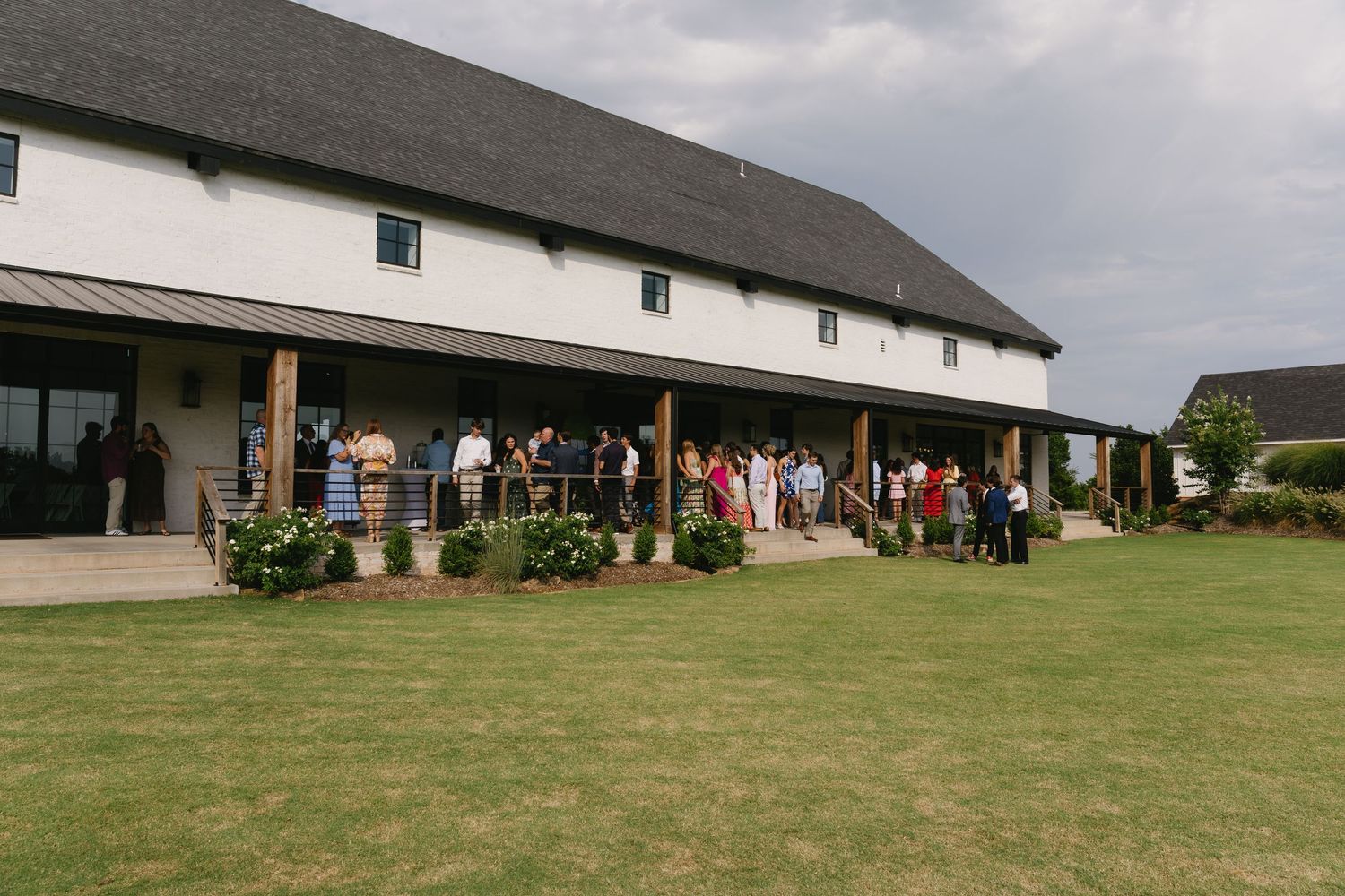 Long white barn-style building with green lawn and gathering of people outside.