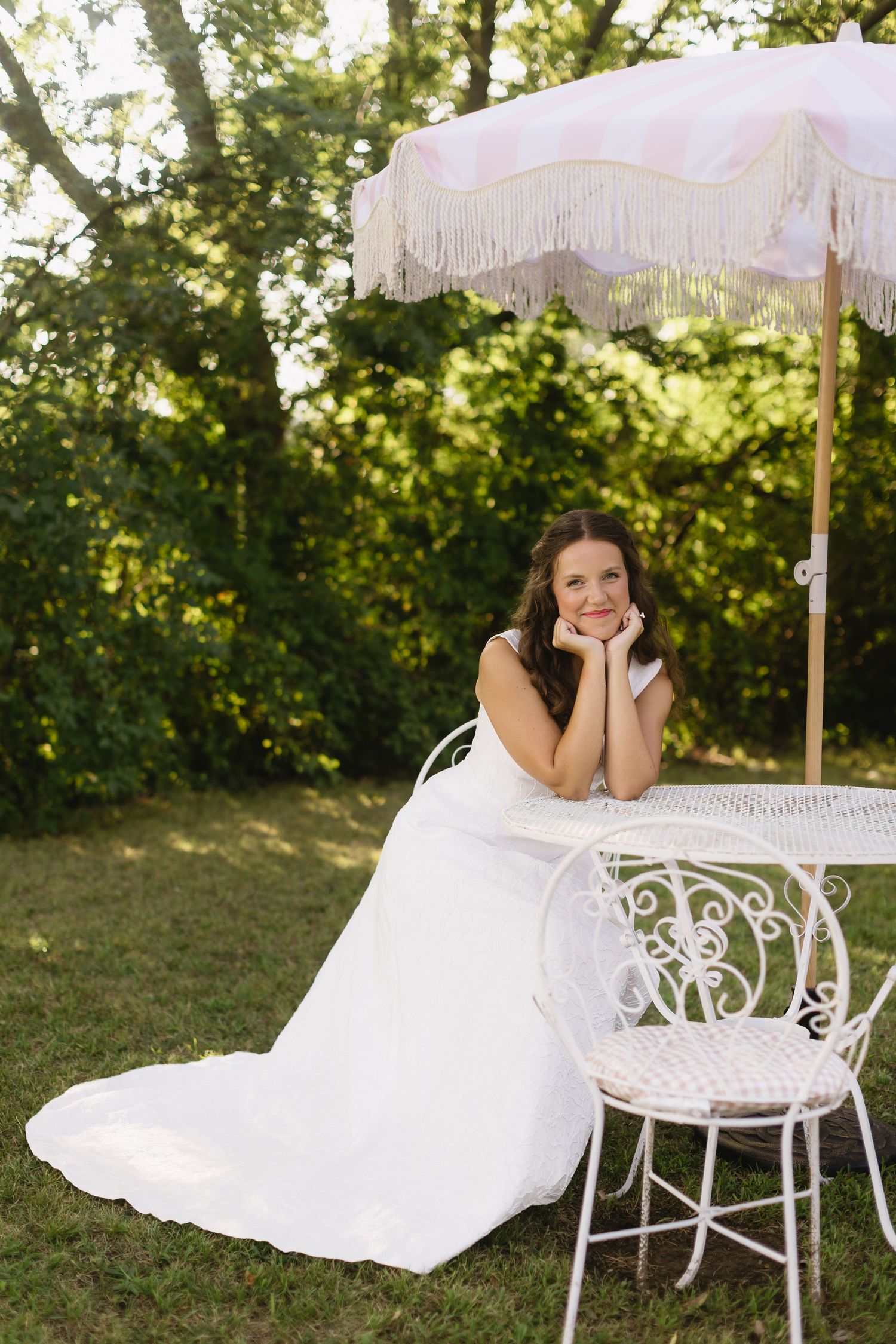 A bride poses playfully at an elegant outdoor tea party setting with white furniture.