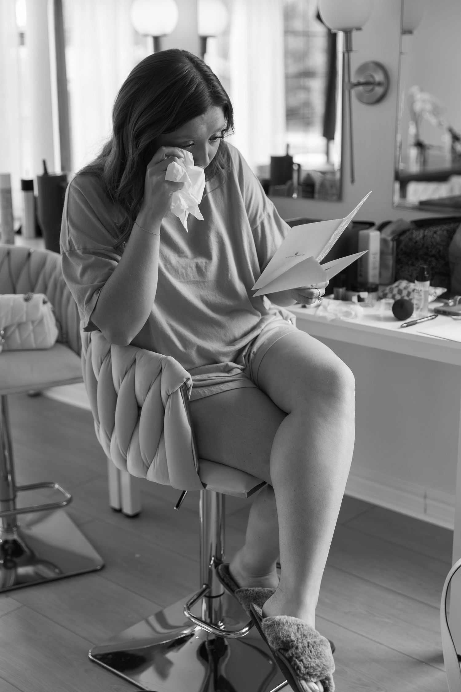 Black and white image of person reading while seated on quilted vanity chair.