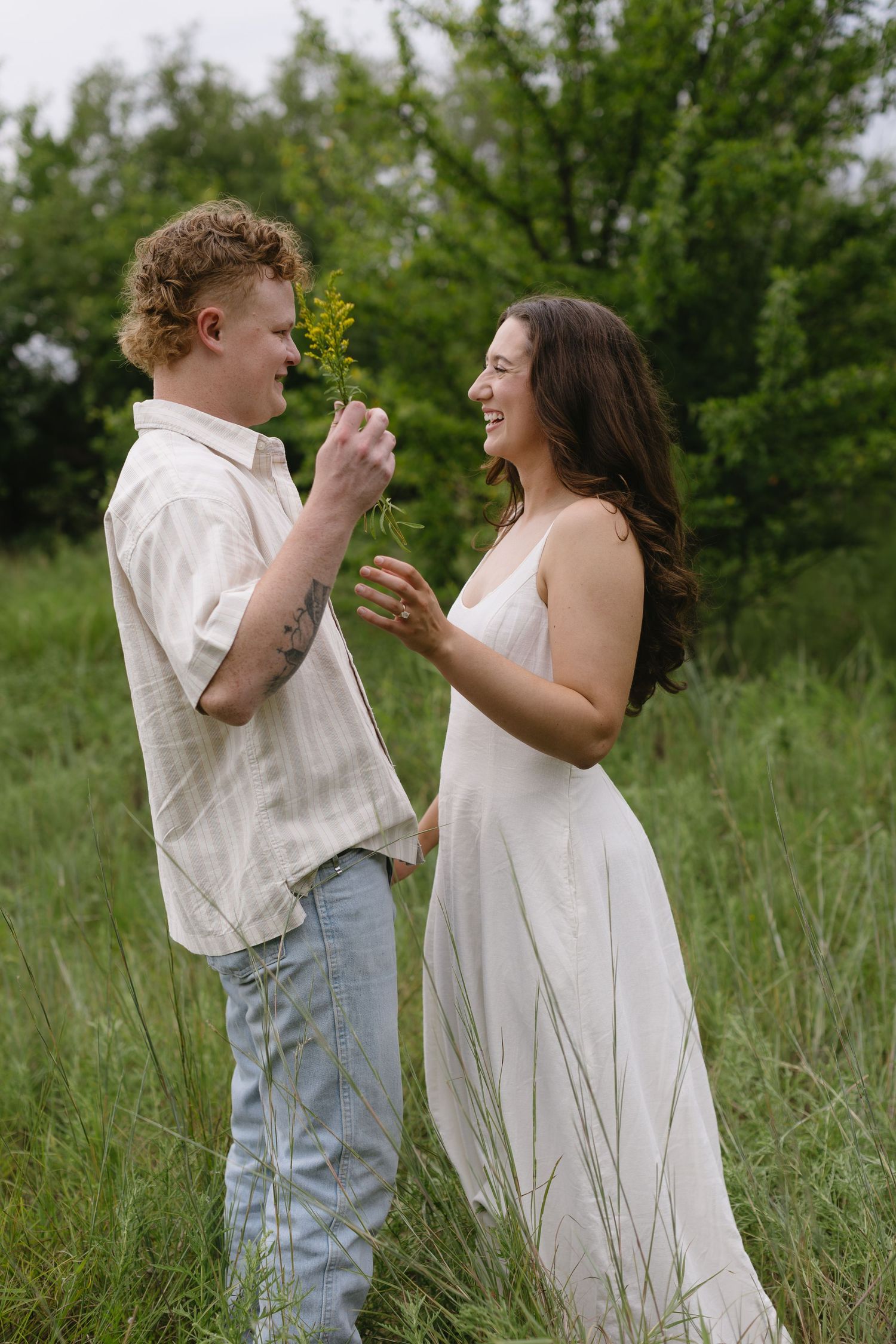 Two people in white outfits share joyful moments while standing in tall grass.