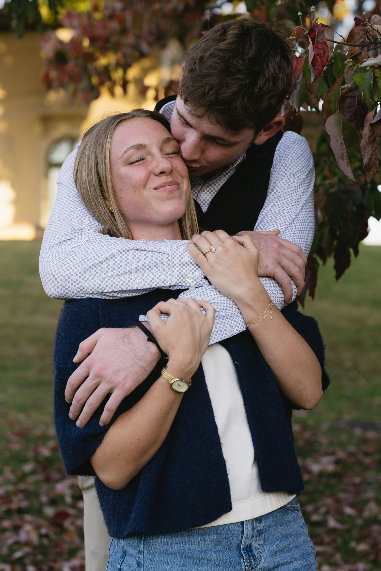 A tender moment captured between a couple hugging outdoors near autumn foliage.