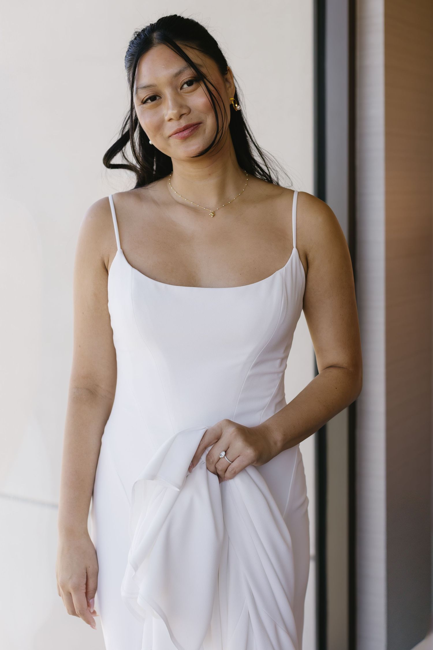 A white spaghetti strap dress is displayed against a minimalist interior background.