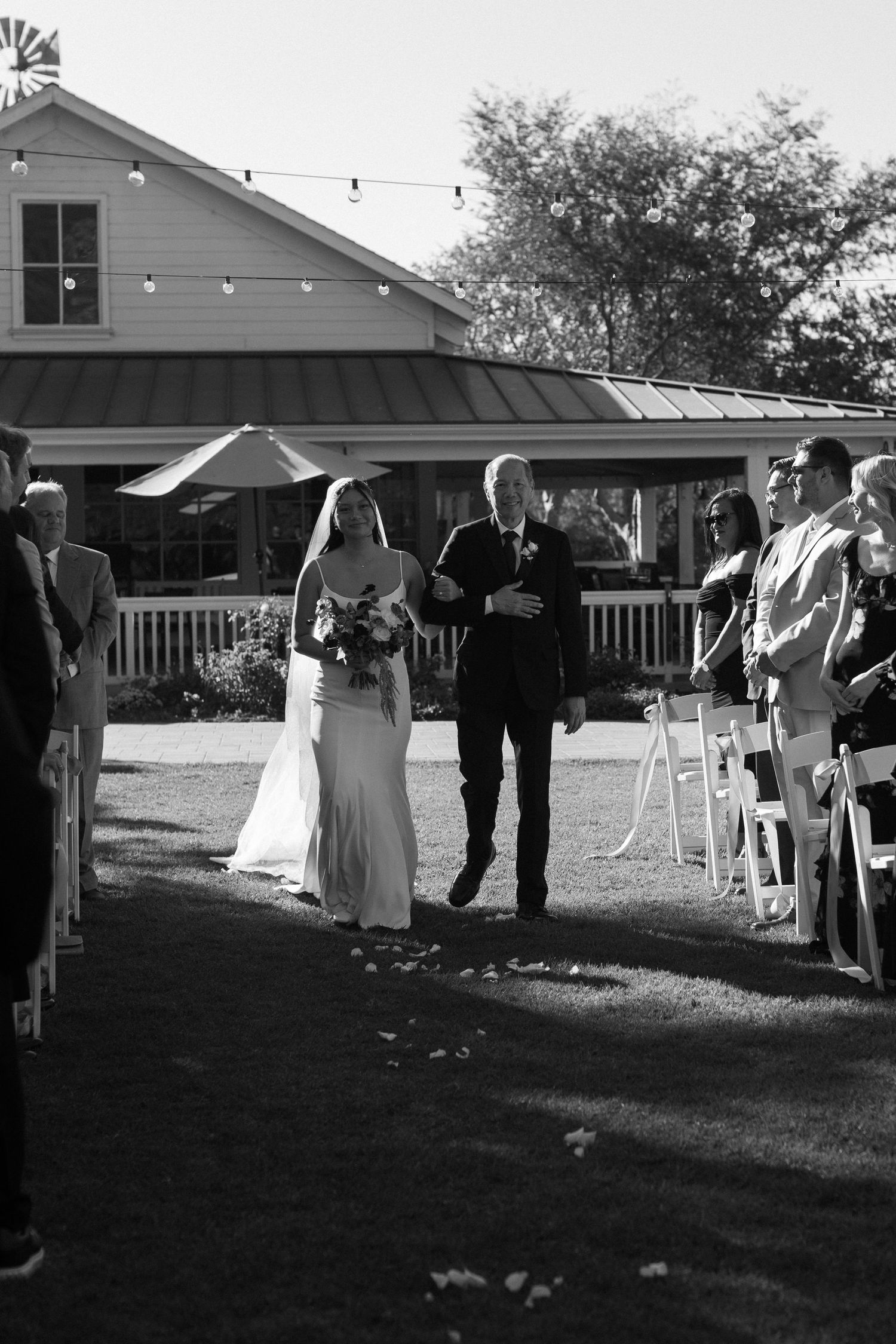 Outdoor wedding ceremony setup with white chairs and string lights at dusk.
